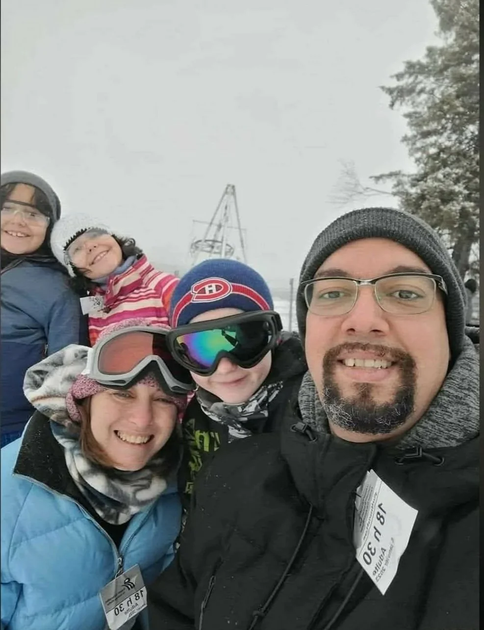 Groupe de cinq personnes souriantes, habillées pour le ski, en forêt enneigée avec un appareil d'observation au fond.