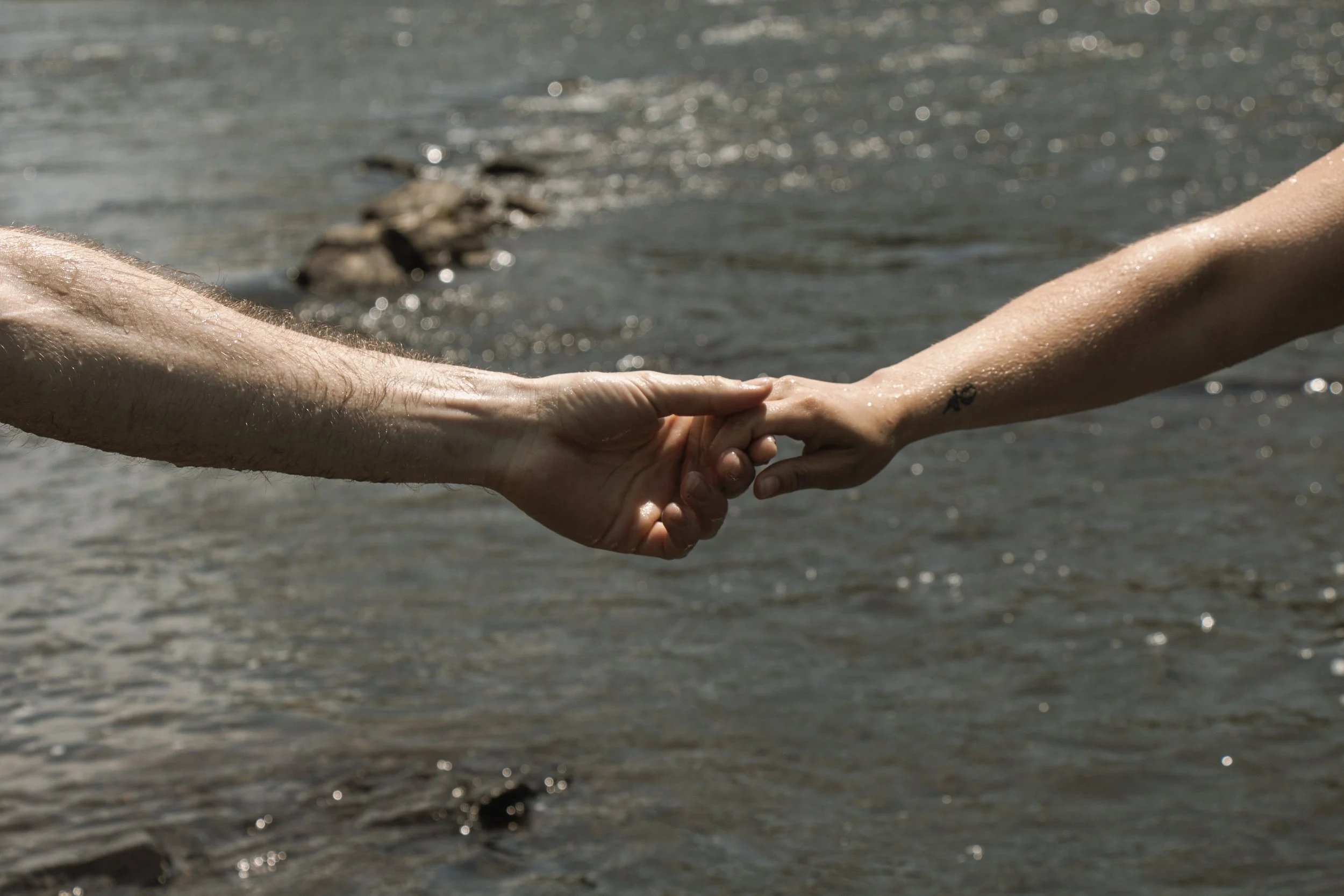 Close-up of two hands holding each other near a body of water.