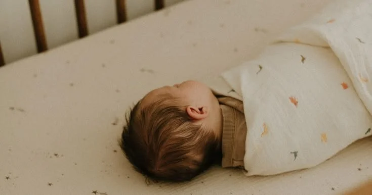A baby sleeping peacefully in a crib, covered with a colorful blanket.