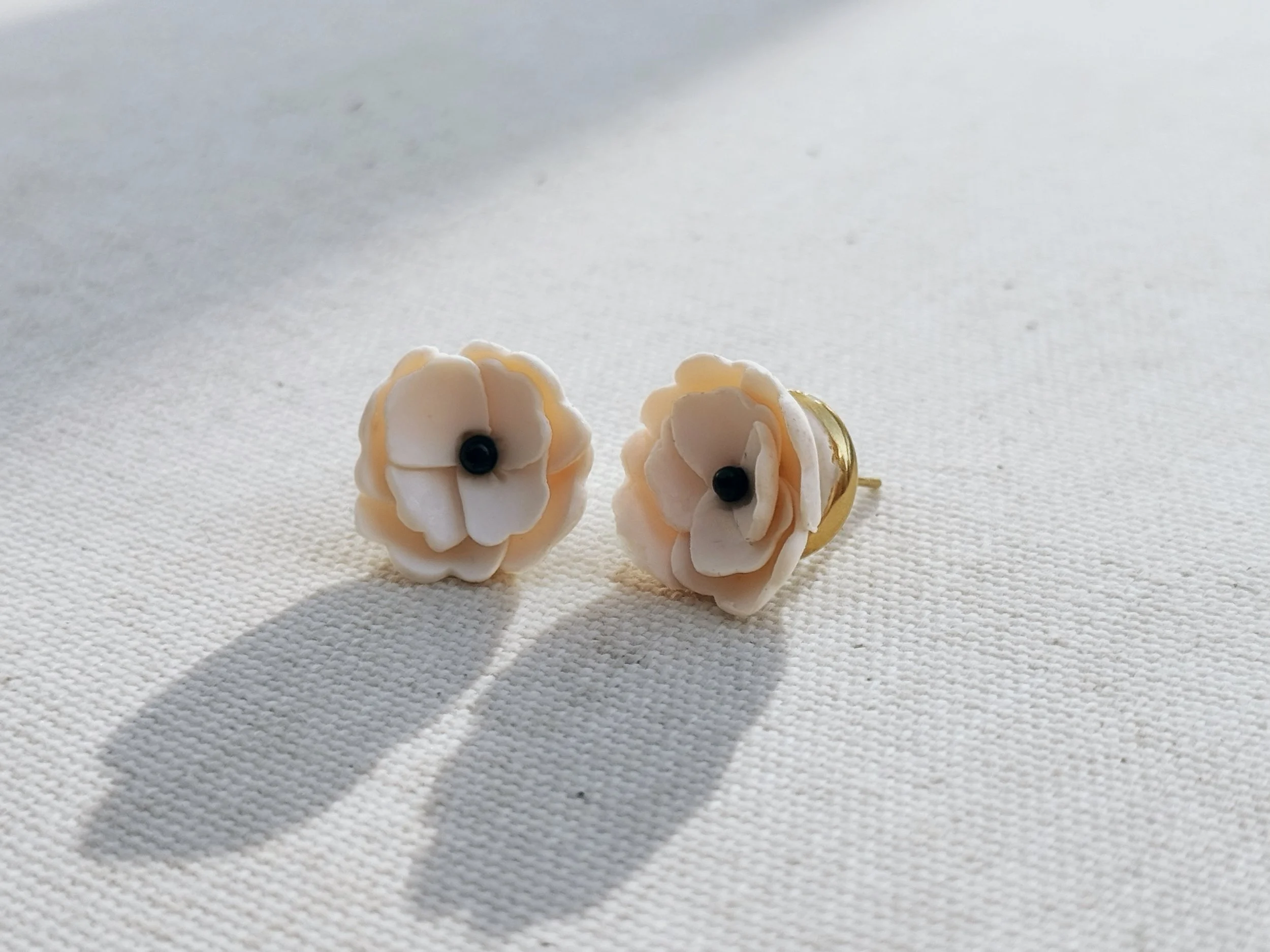 Pair of flower-shaped earrings with white petals and black centers on a white textured surface.