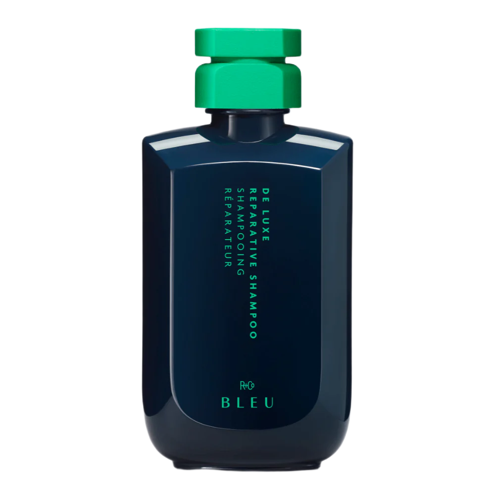 A dark blue bottle with a green cap containing De Luxe Reparative Shampoo, Shampooing Restructurant Repareteur, in a minimalist design.