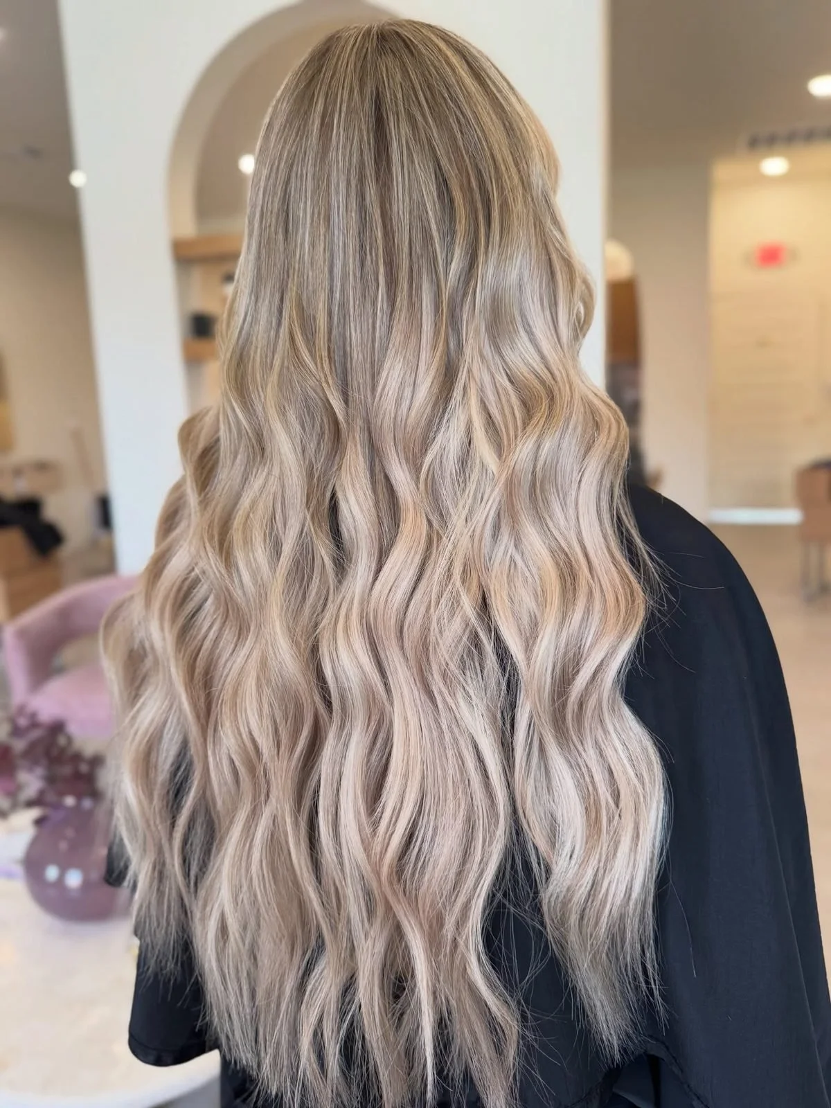 Long wavy blonde hair extensions blended seamlessly into natural hair at a Tomball, TX hair salon.