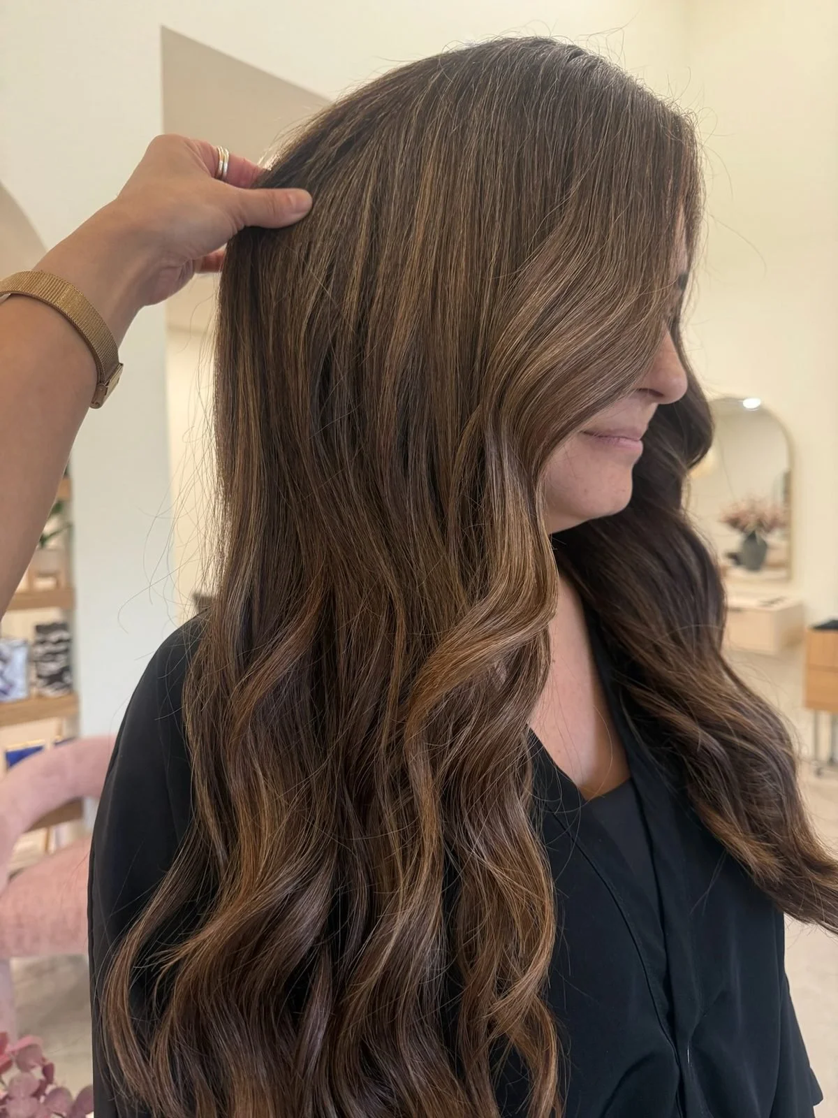 Stylist lifting a section of brunette hair to check extension bonds at a hair extension maintenance appointment in Tomball, TX.