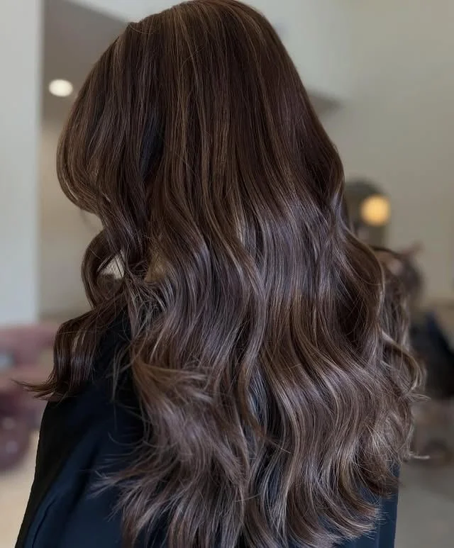 Lived-in brunette hair color with a soft shadow root and caramel dimension, styled in loose waves in Tomball, TX.