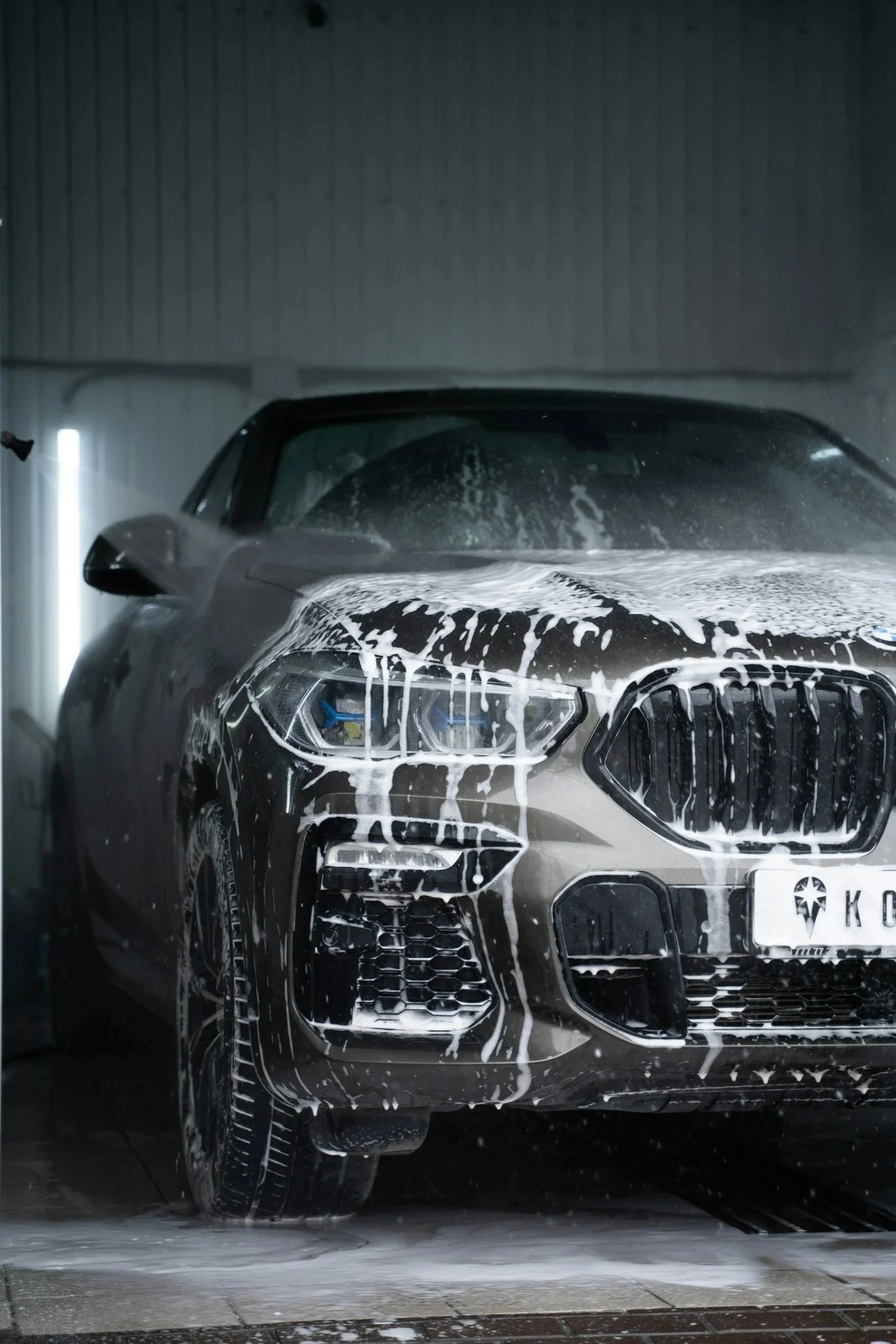 Black car being washed with soap and water in a car wash bay.