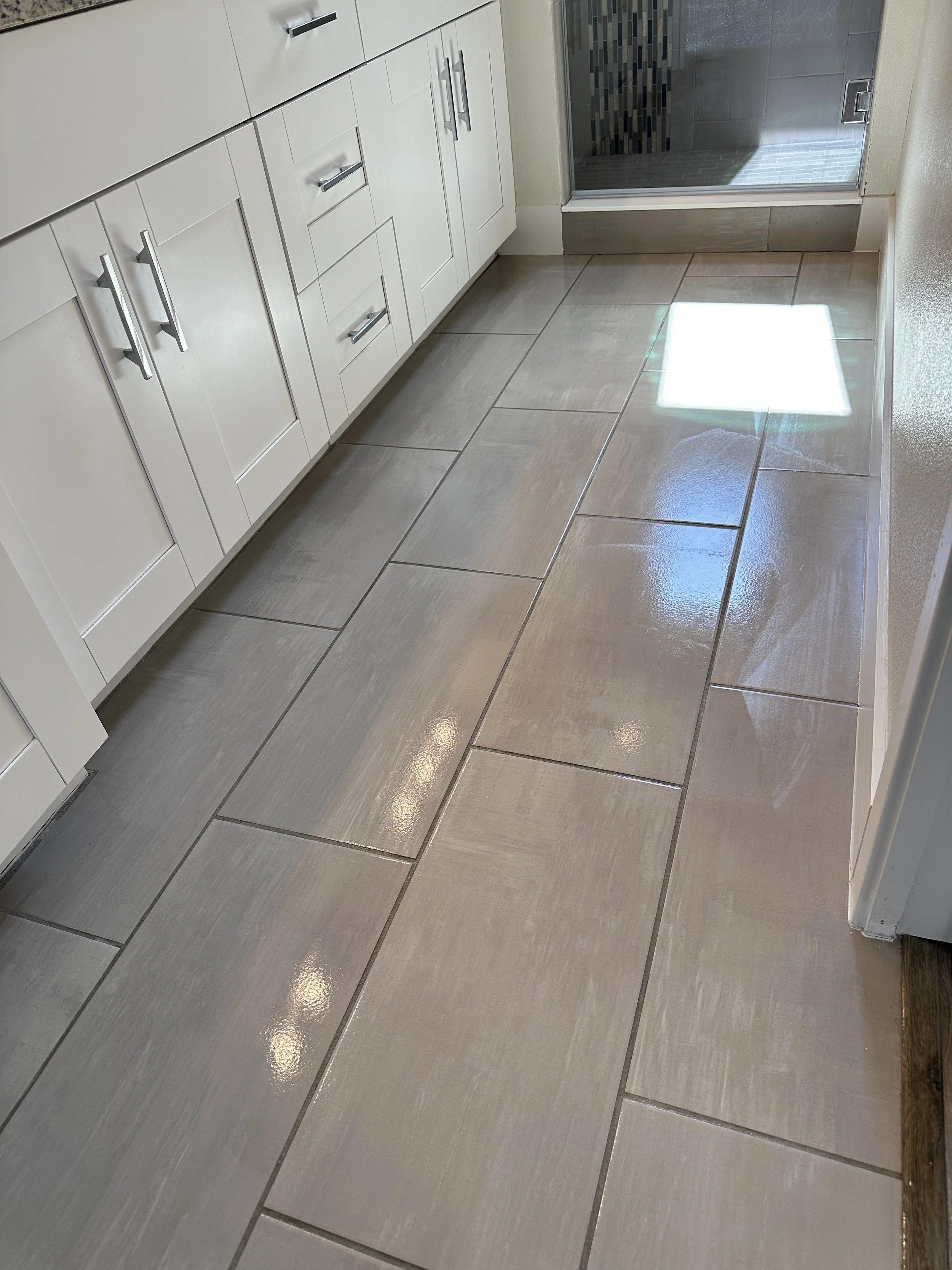 A bathroom with white cabinets, beige tiled flooring, and a glass shower door with a tiled interior.