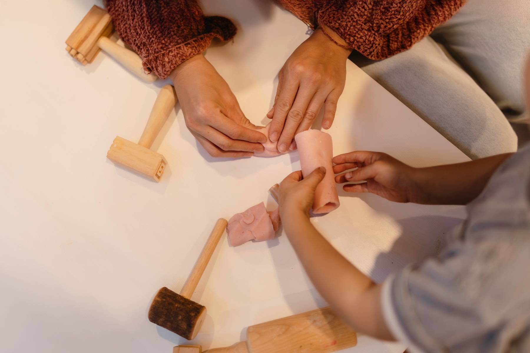 People rolling out dough with wooden rolling pins on a white surface.