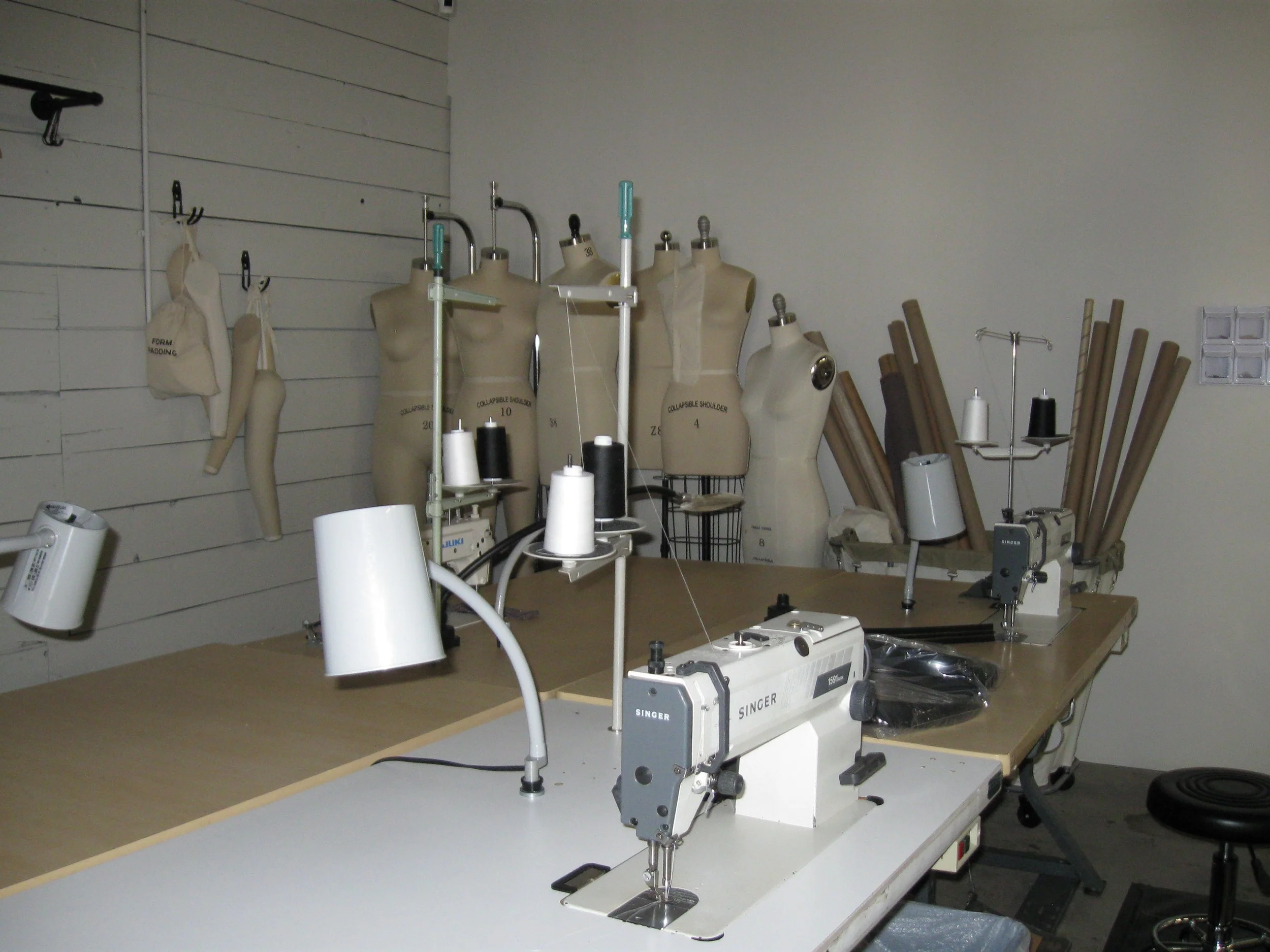 A sewing workshop with mannequins, sewing machines, and fabric rolls on a table.