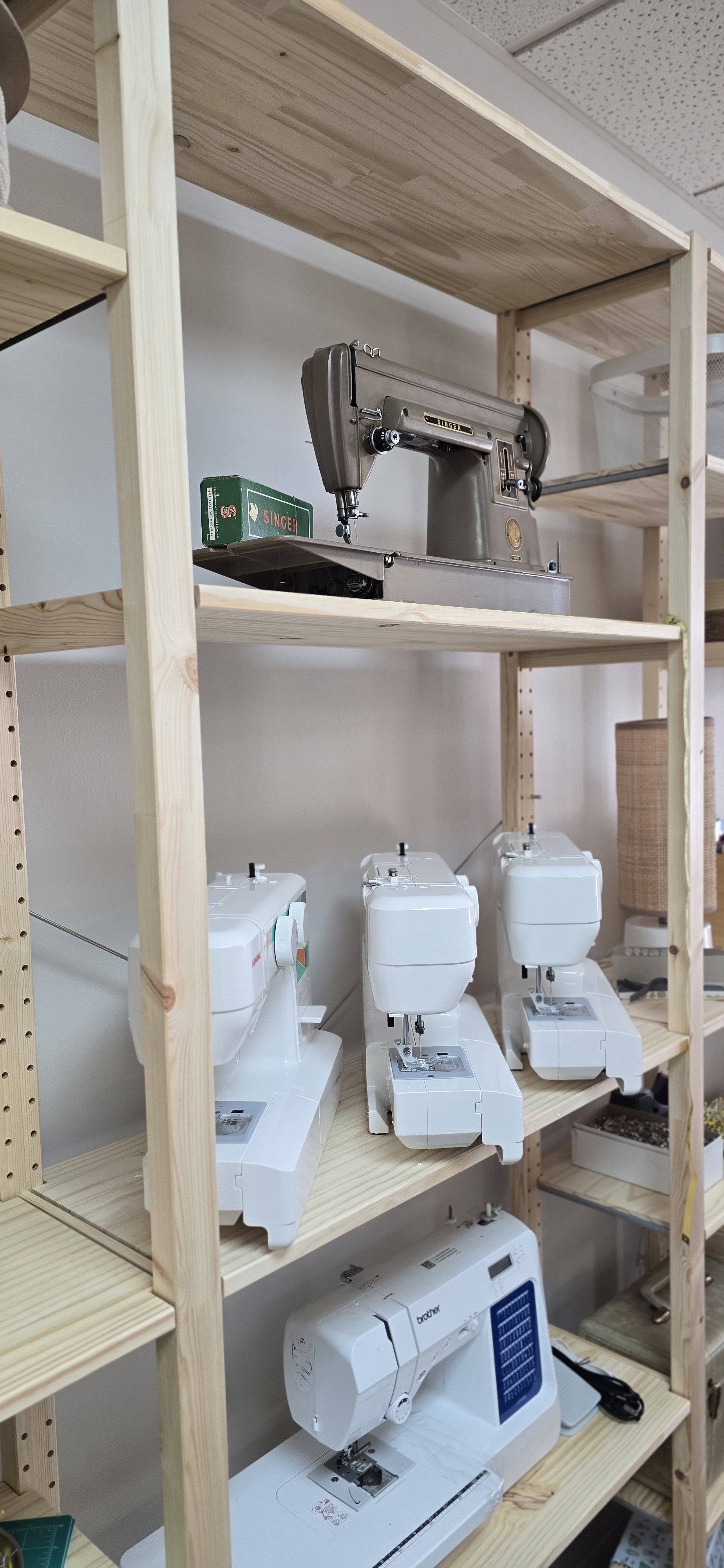 Vintage singer sewing machine on top shelf with domestic Janome sewing machines on the lower shelf