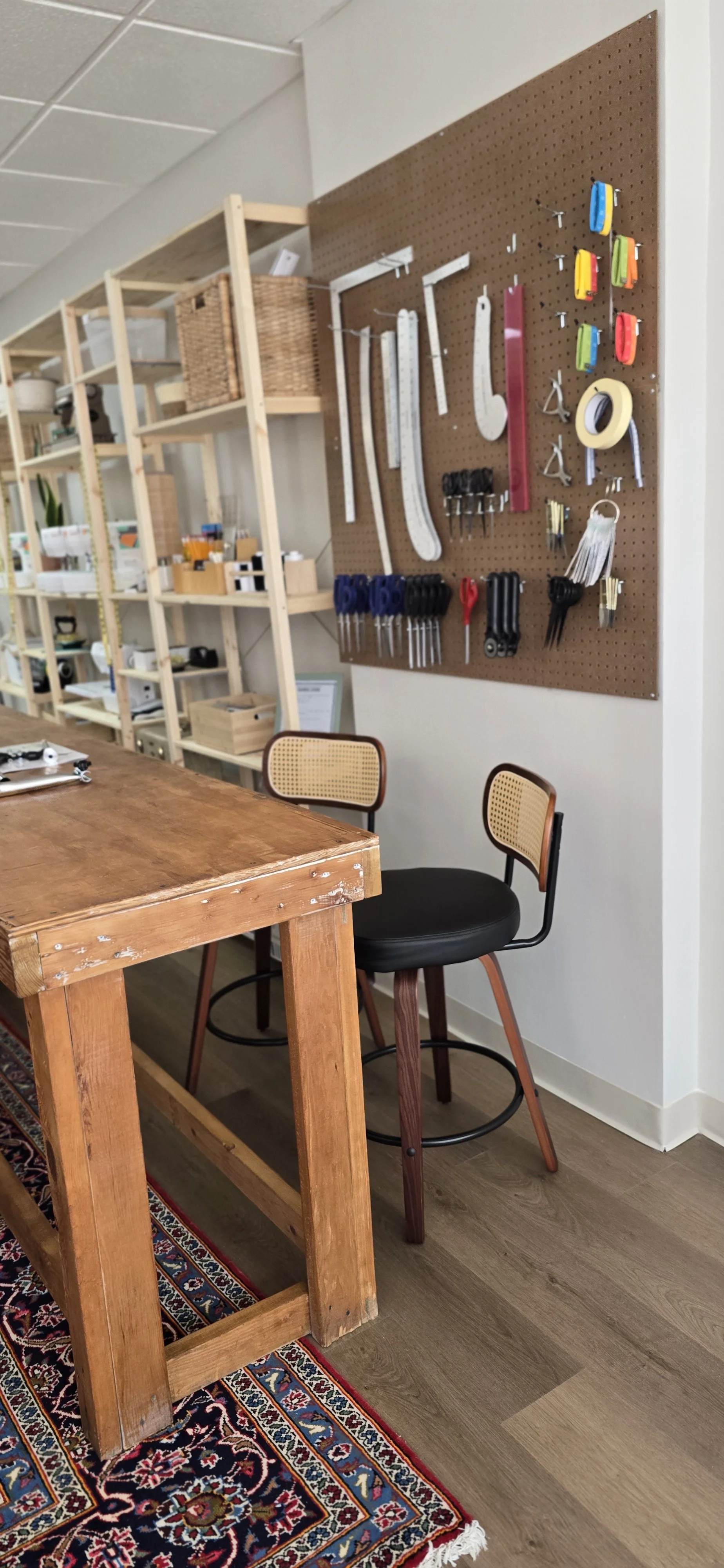 A workshop corner with a pegboard holding various tools and supplies, a wooden worktable, and two chairs with woven cane backrests.