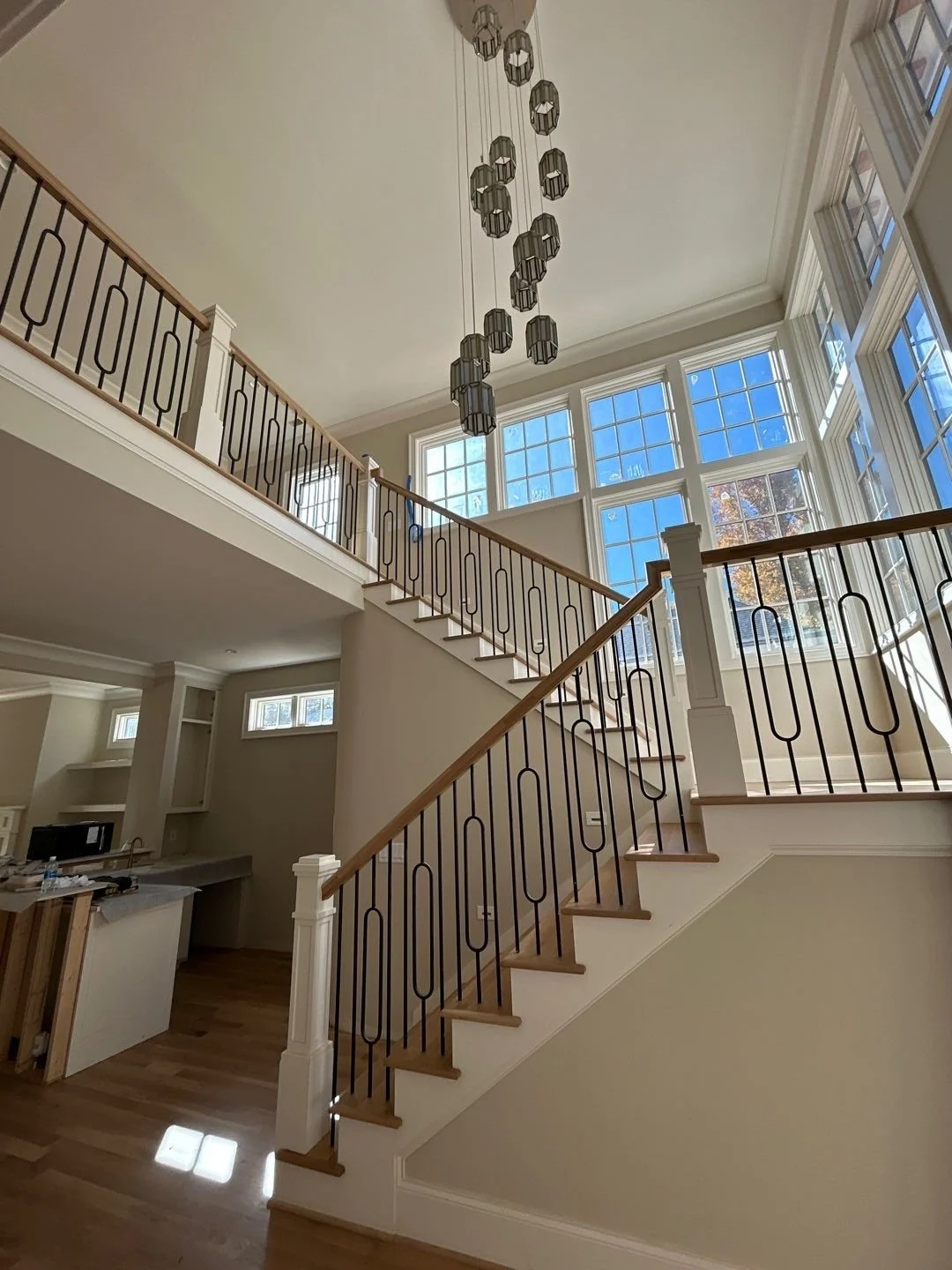Interior view of a spacious, multi-story home with a staircase, large windows, and a modern chandelier.
