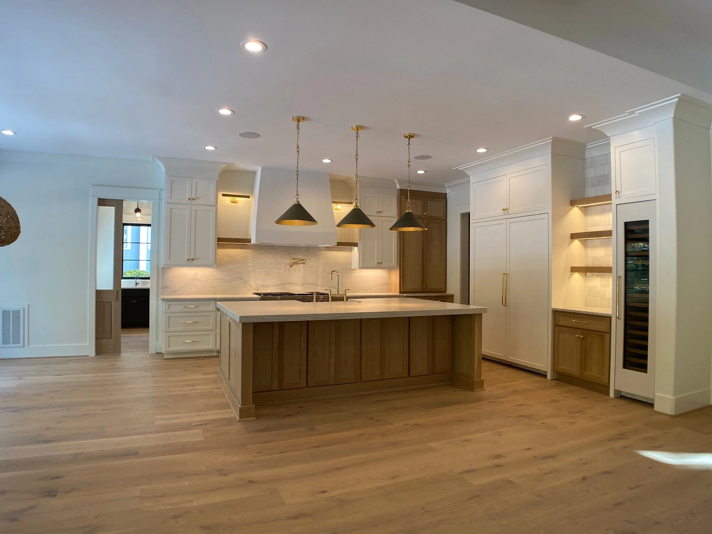 Modern kitchen with white cabinets, a kitchen island, pendant lights, and wood flooring.