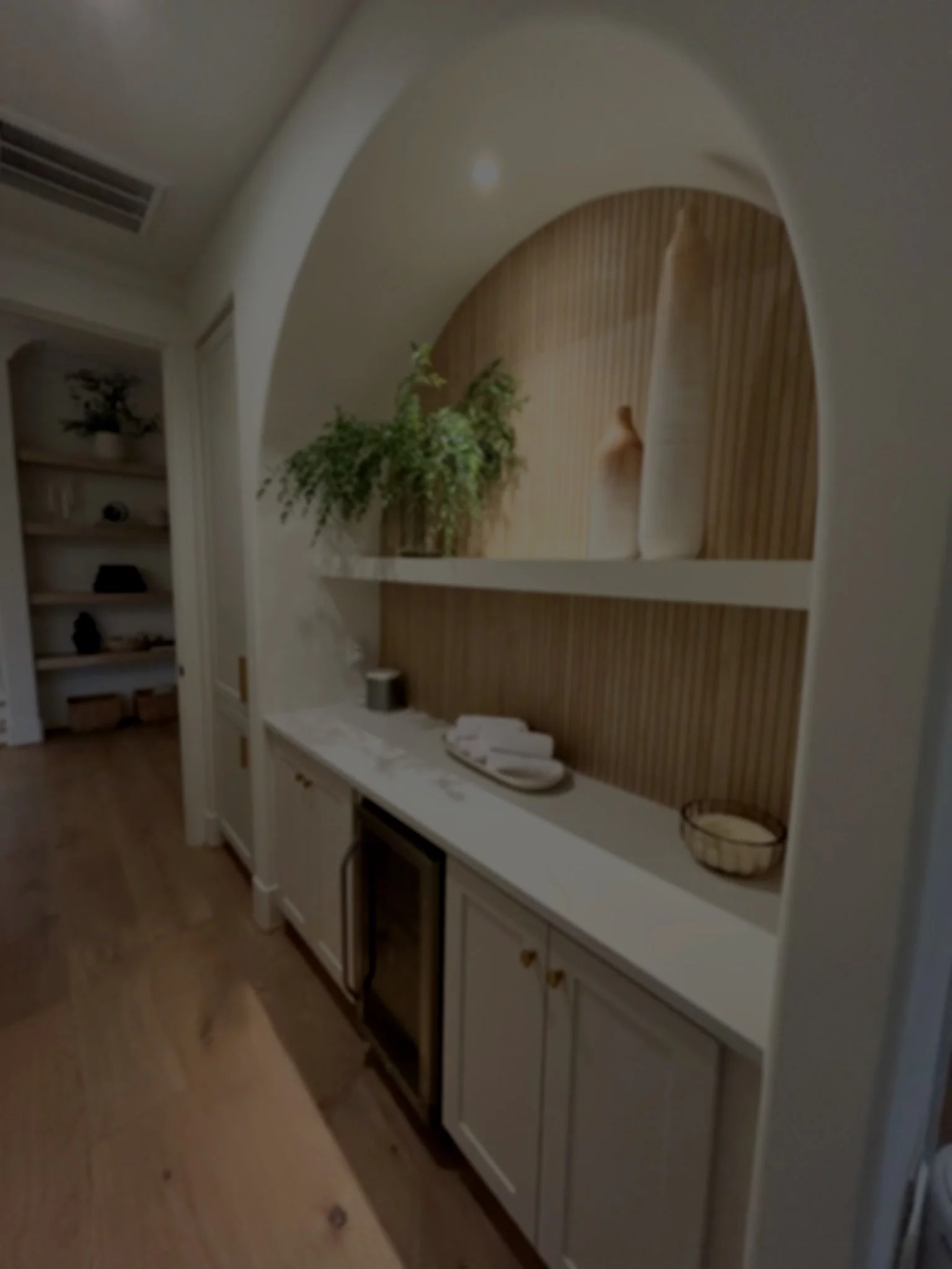 Interior view of a built-in white cabinet with a wooden backsplash, two shelves displaying decorative items, and a countertop with a few folded white towels and a small woven basket.