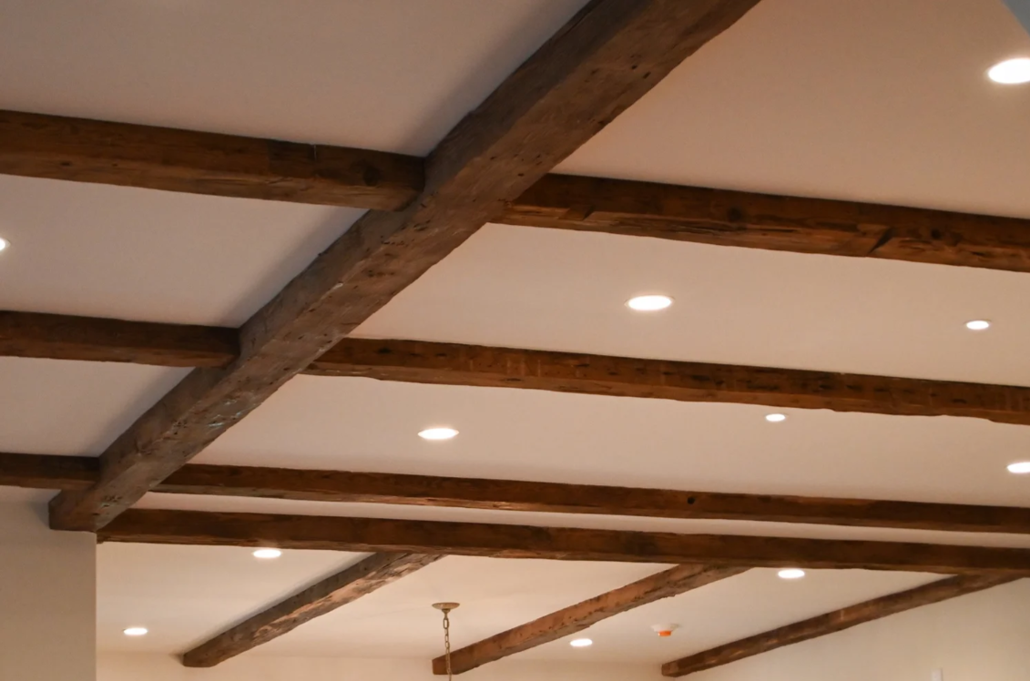 Ceiling with wooden beams and recessed lighting in an interior space.