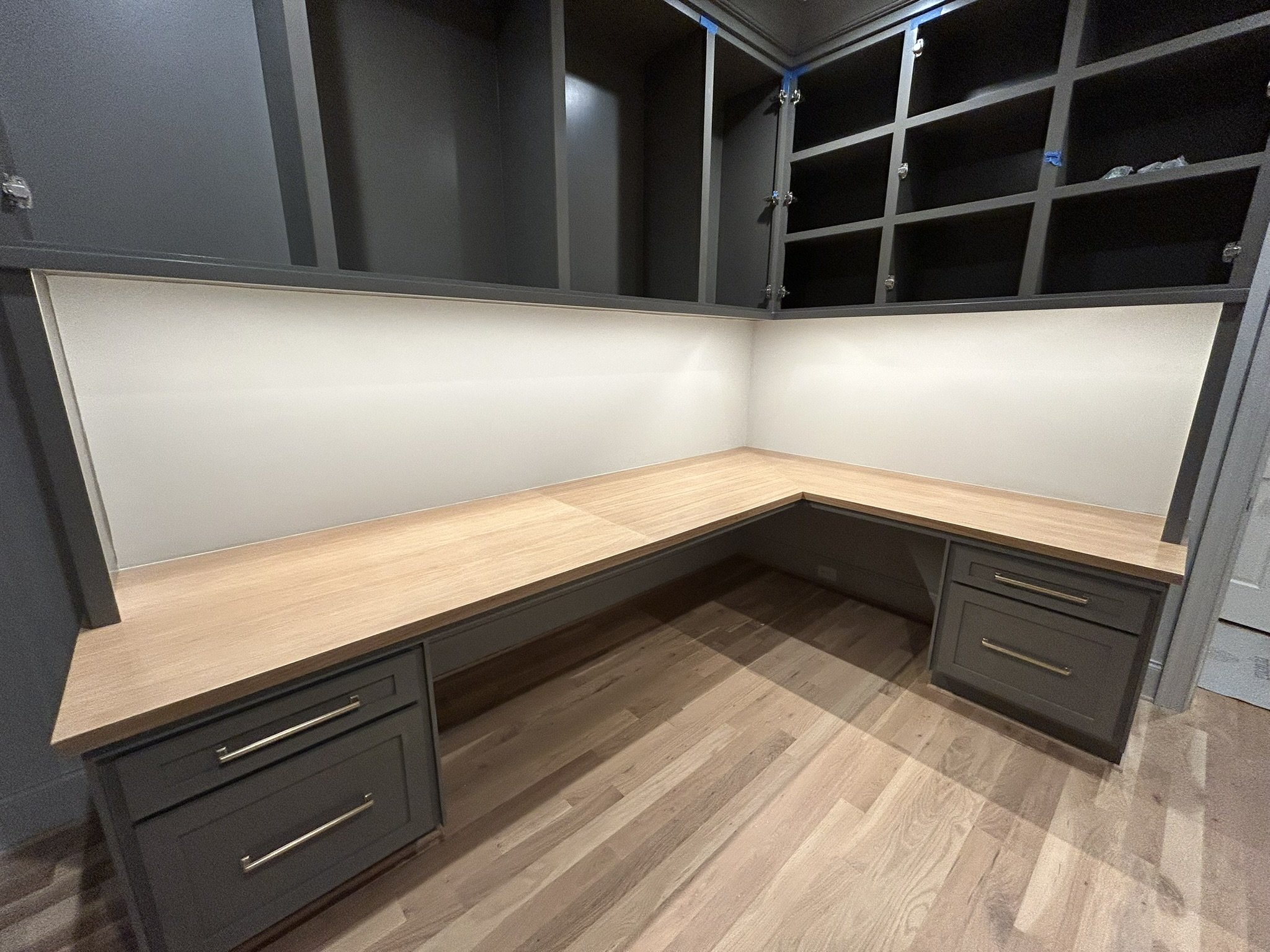 Corner L-shaped desk with black cabinetry and a wood top, with multiple cubby storage compartments above and drawers below.