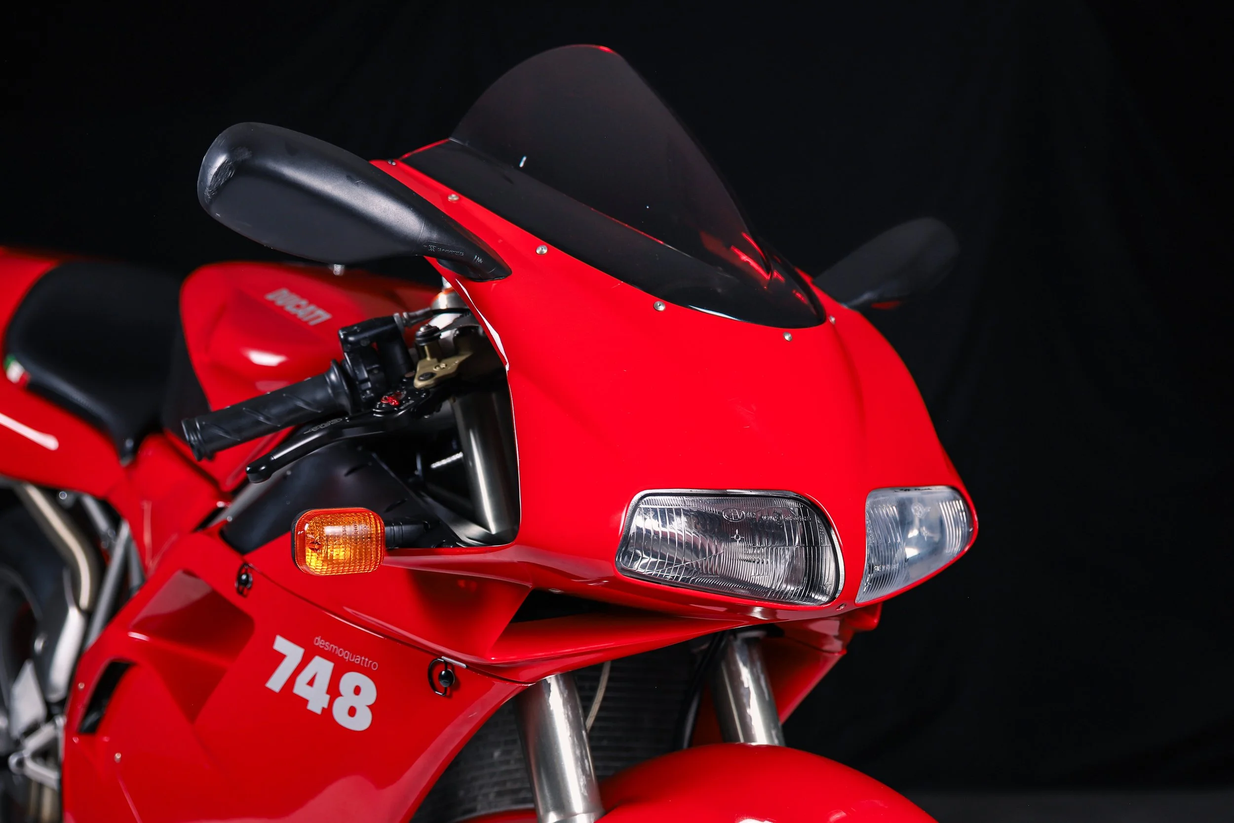 Close-up of a red racing motorcycle with a black windscreen, handlebar, and headlight against a dark background.