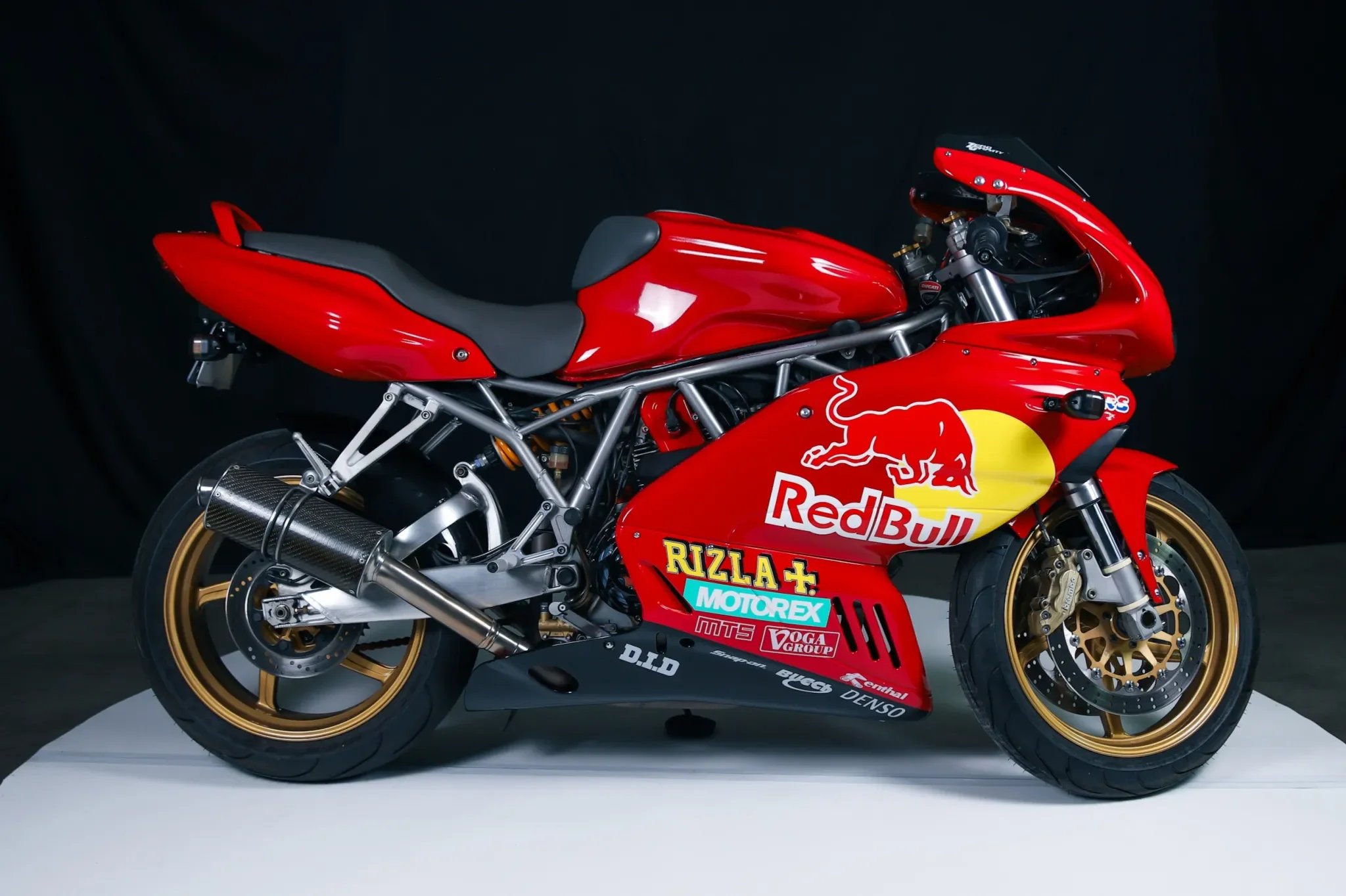 Red racing motorcycle with various sponsor decals, gold wheels, and a black background.