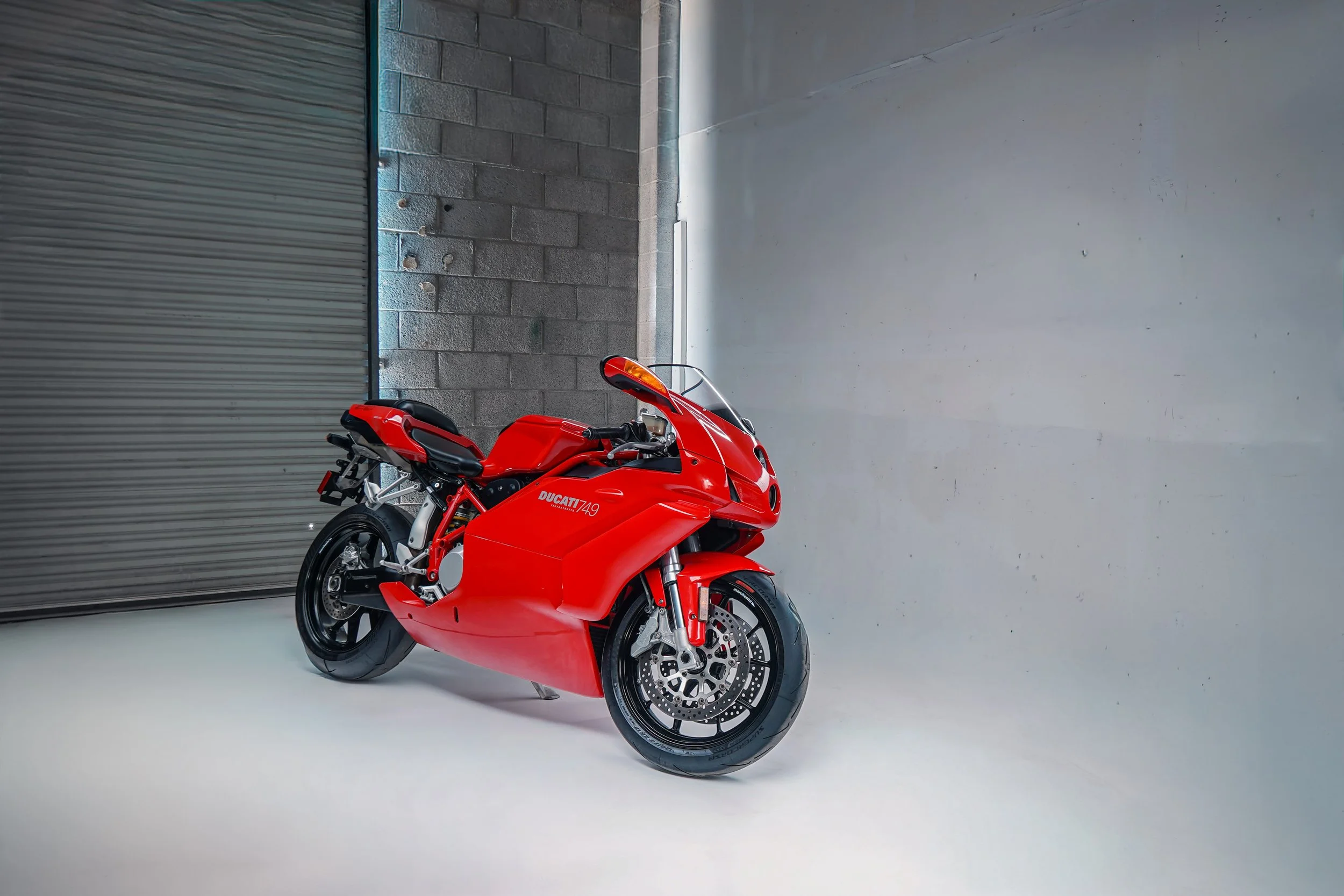 Red Ducati sport motorcycle parked indoors against a gray wall and gray garage door in a minimalist setting.