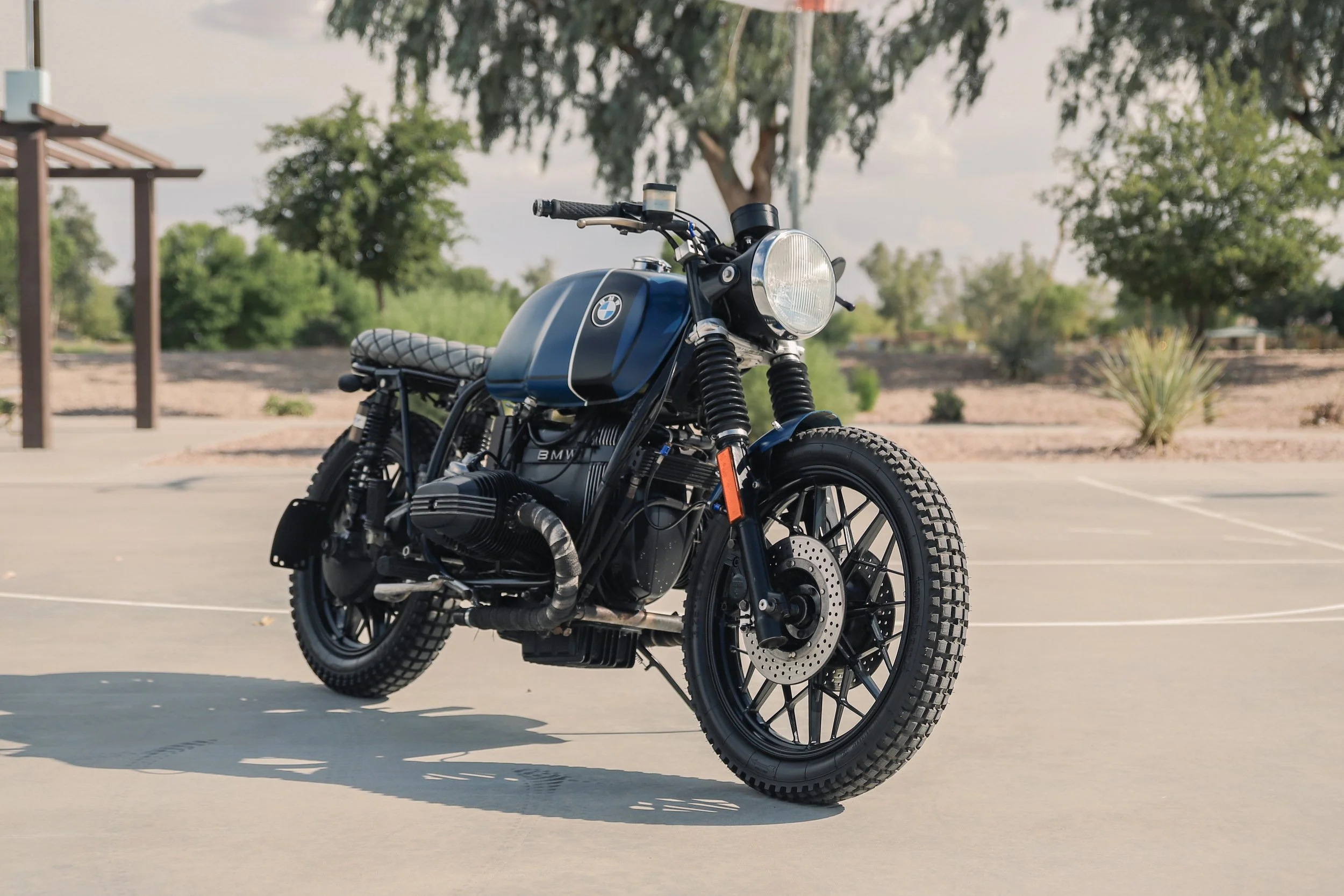 A black vintage BMW motorcycle parked outdoors on a concrete surface with trees and a blue sky in the background.