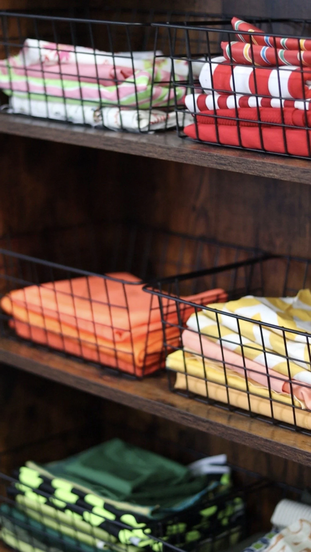 Fabric inside four wire baskets on wooden shelves, with various colors and patterns.