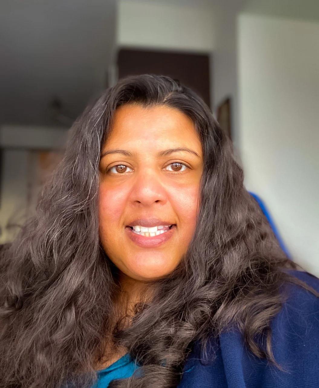 Close-up of a woman with long, wavy brown hair smiling indoors.