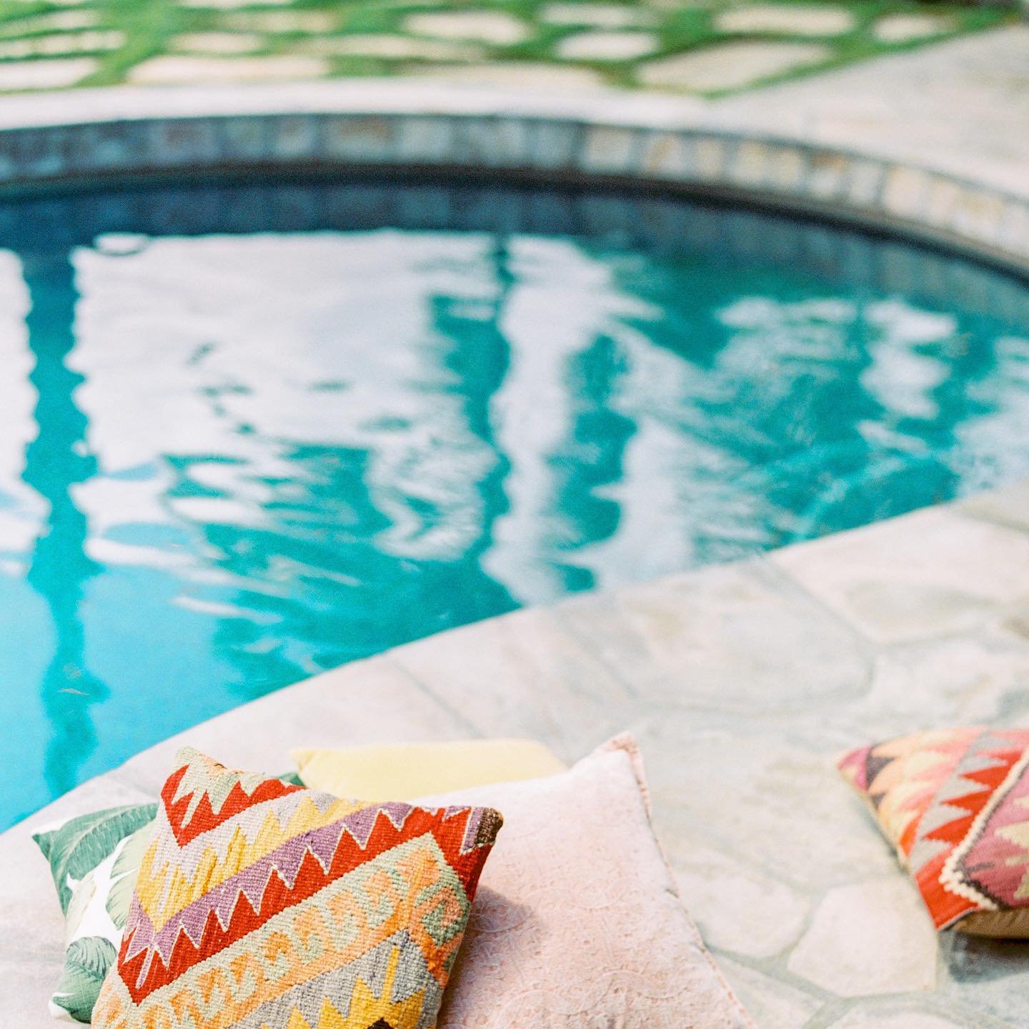 A close-up view of a swimming pool with colorful patterned pillows placed on the poolside.