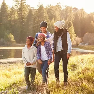 Four friends walking together outdoors in a scenic park by a lake, enjoying a sunny day.