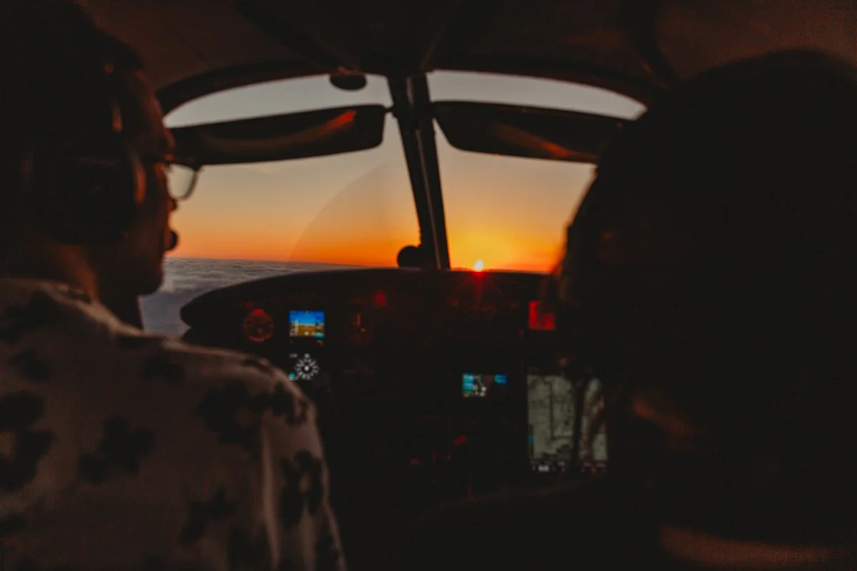 Cockpit of a small airplane with two pilots flying during sunset over the ocean.