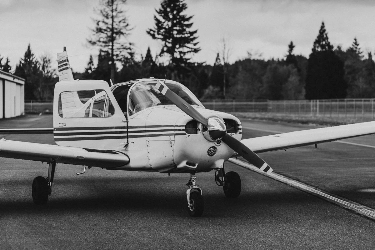 A small twin-engine airplane parked on a tarmac with trees and a fence in the background.