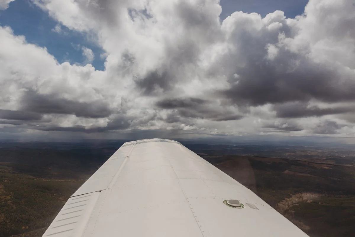 A view from the cockpit of a small airplane flying above a landscape with cloudy skies.