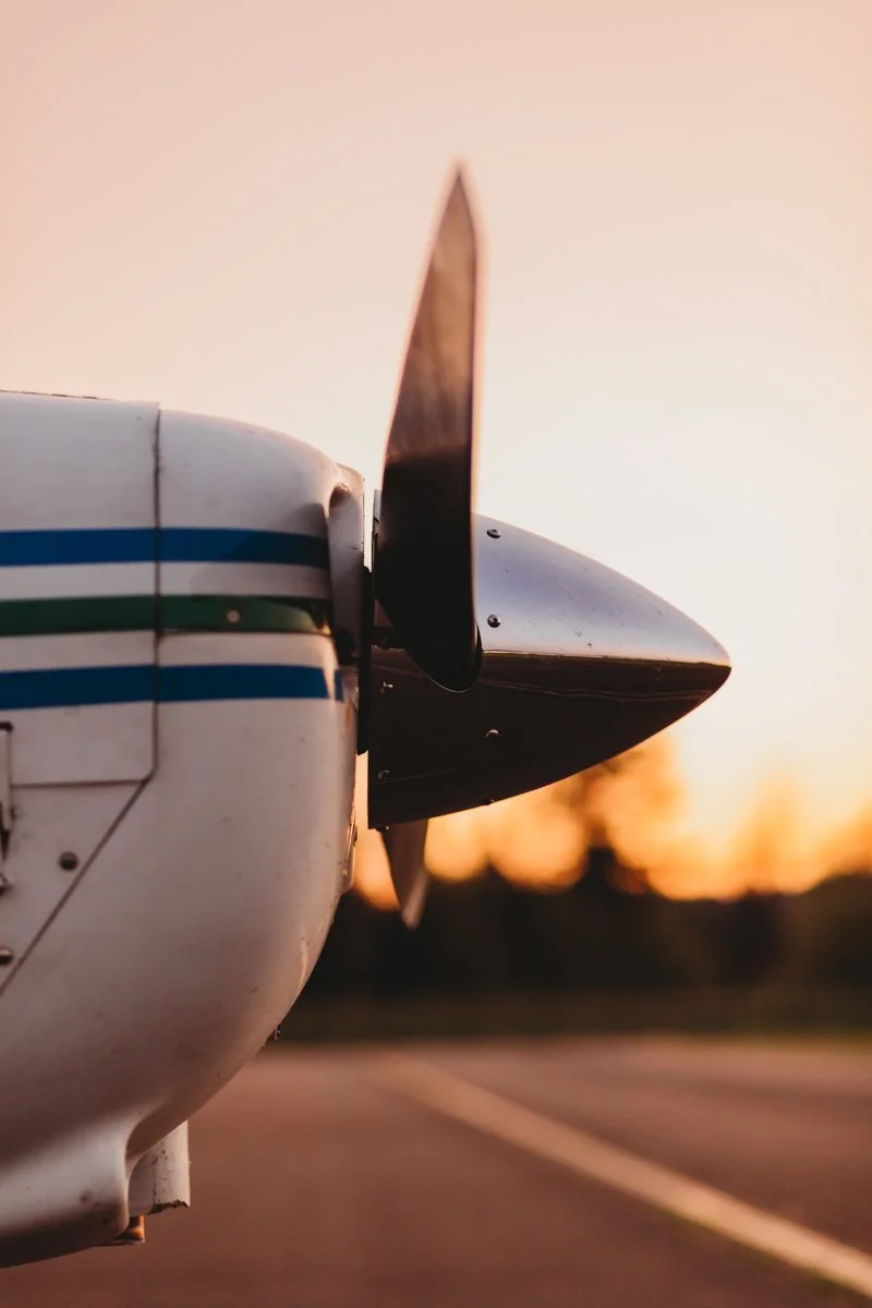 Close-up of the nose and propeller of a small airplane on a runway at sunset.