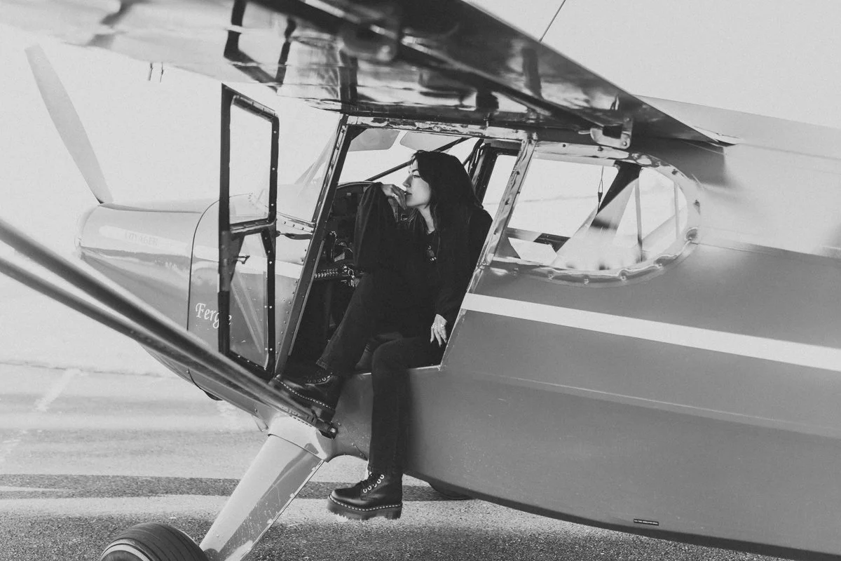 A person sitting in the cockpit of an aircraft, with one leg hanging out, in black and white.