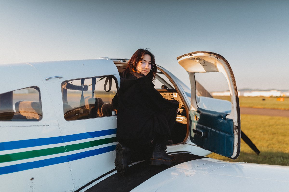 Woman with glasses sitting in the cockpit of a small airplane on the tarmac at sunset