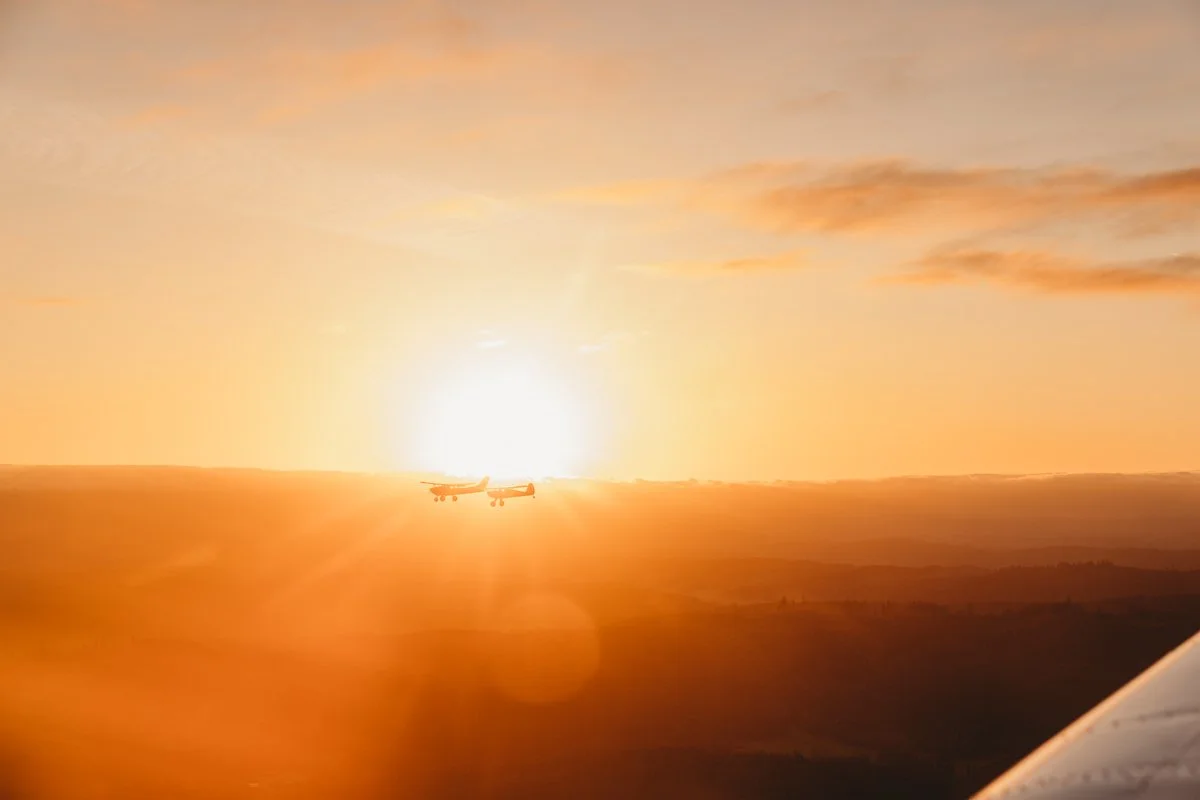 Two airplanes flying during a sunset sky, with orange and yellow hues and a few scattered clouds.