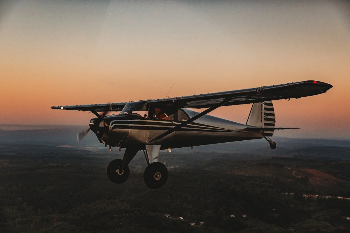 Small propeller airplane flying during sunset over a green landscape.