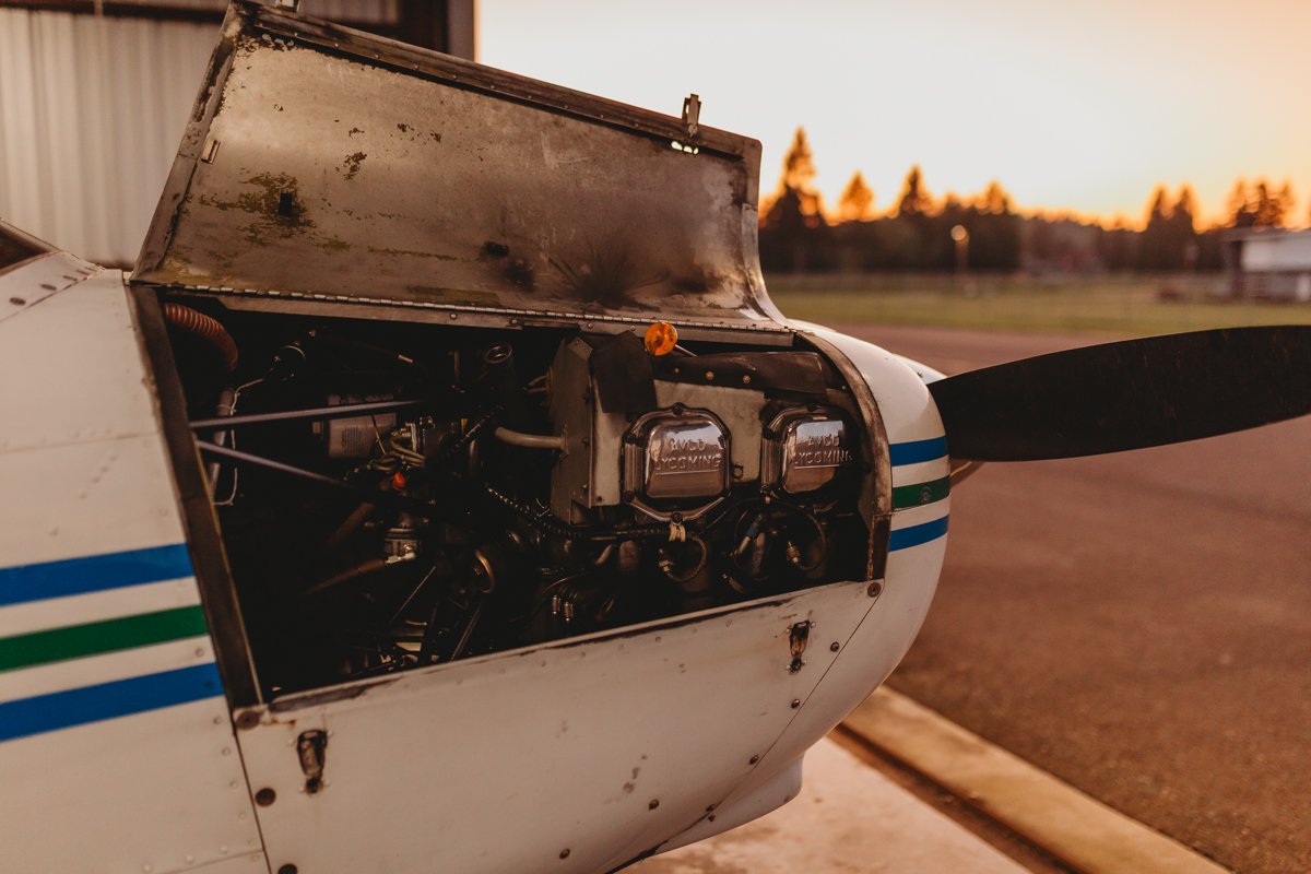 Close-up of the open engine compartment of a small, white propeller airplane with blue and green stripes, at sunset.
