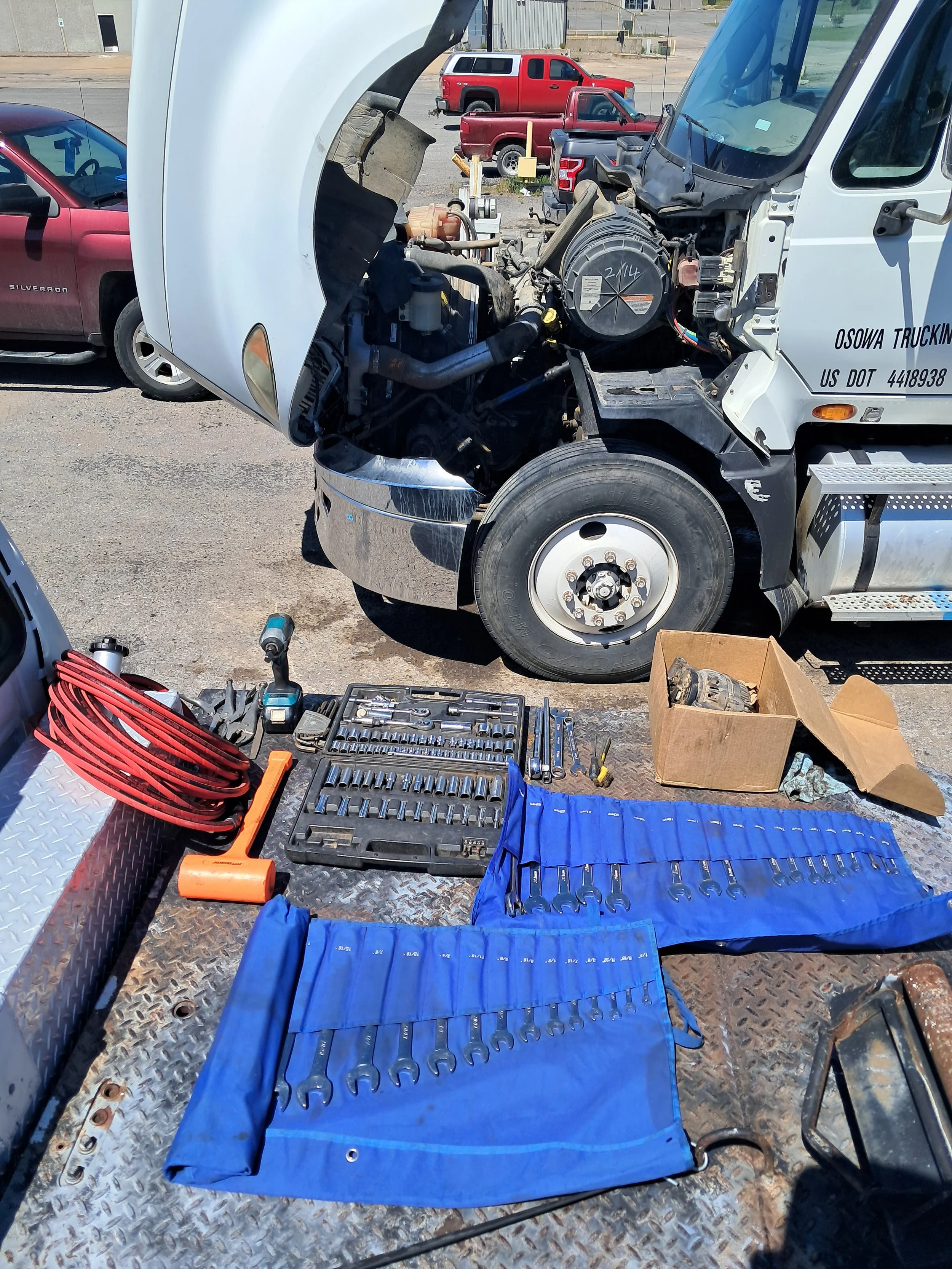 Open semi hood with various tools laid out on a flatbed wrecker service truck, including sockets, wrenches, and other mechanical tools in preparation for an alternator replacement.