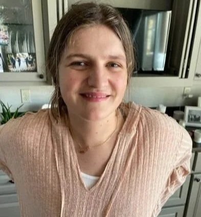 A woman with light brown hair smiling in a kitchen.
