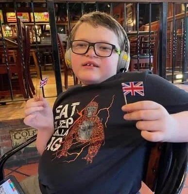 Child with glasses and yellow headphones holding a small British flag at a restaurant or cafe.