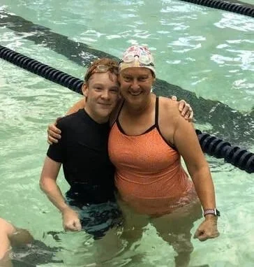 A young boy and a woman in a swimming pool, smiling and hugging each other.
