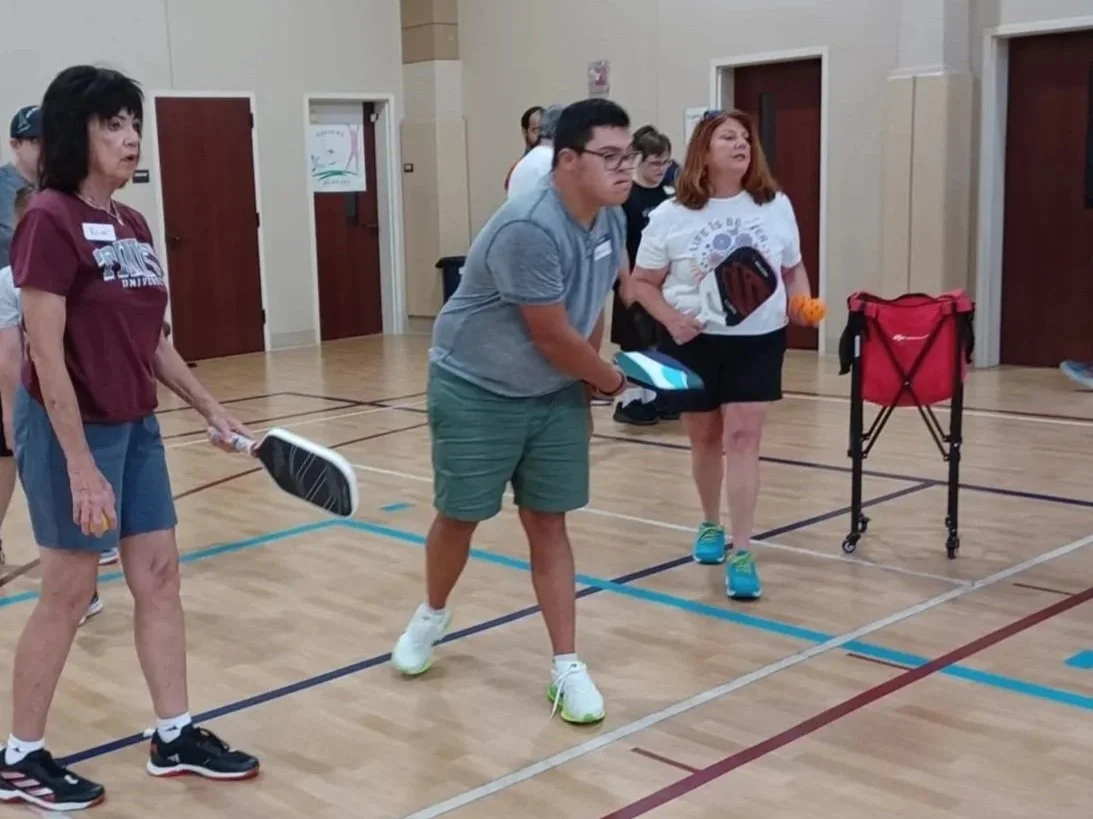 People playing pickleball indoors, holding paddles and standing on a gym floor