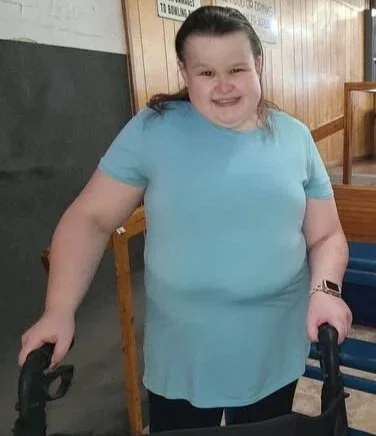 Young girl with a walker smiling in a room with wooden walls.
