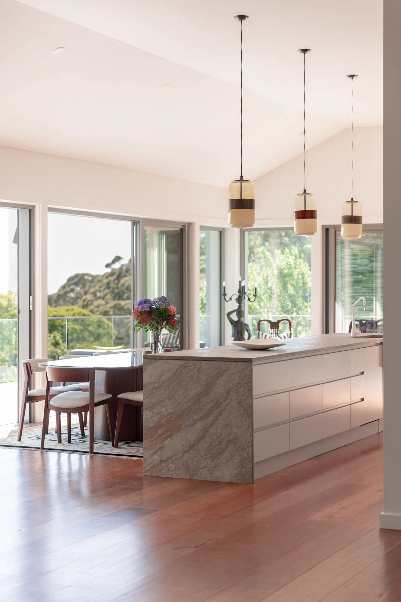 Modern kitchen and dining area with pendant lights, large windows, and a floral centerpiece.