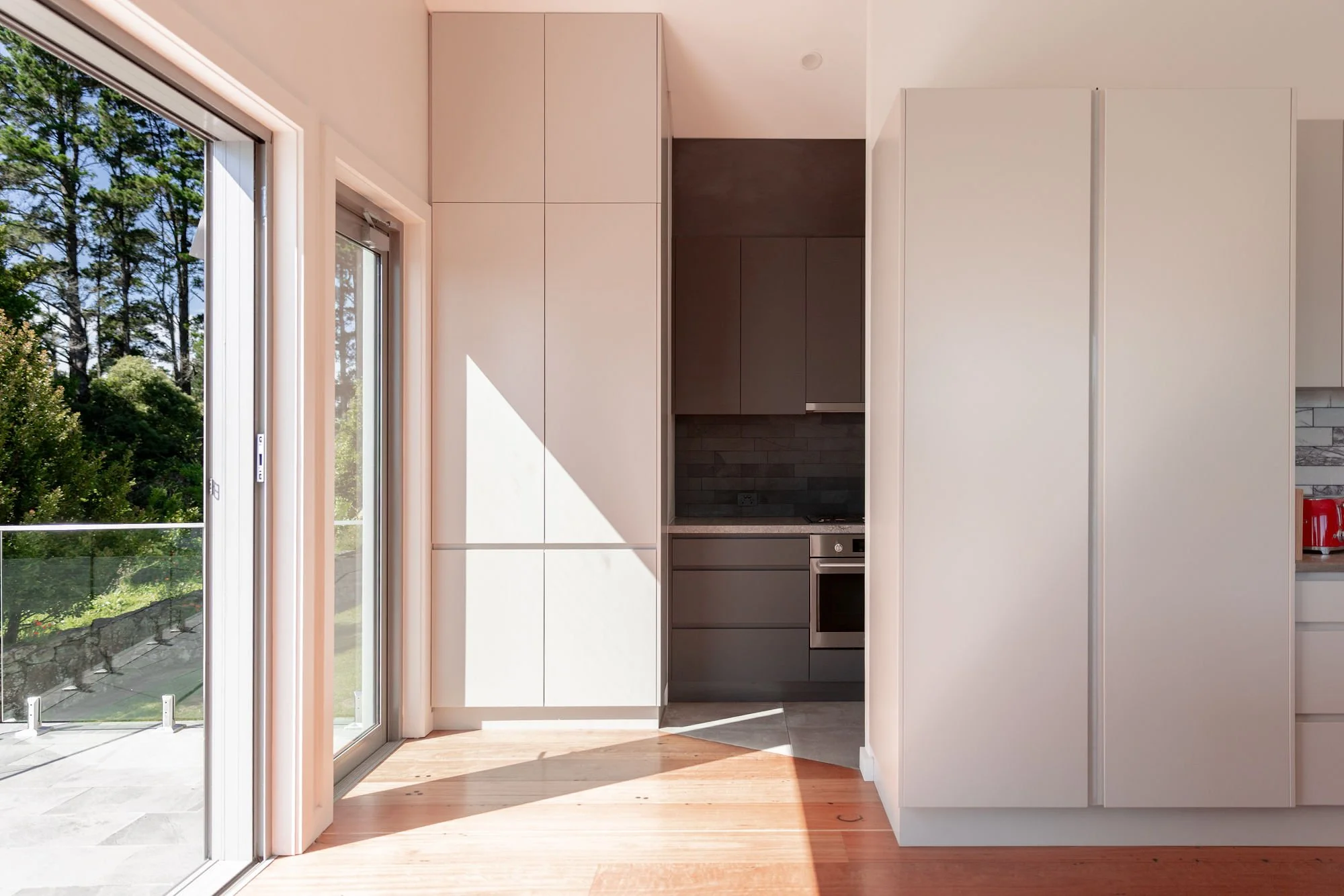 Modern kitchen with large sliding glass doors, white cabinets, dark gray lower cabinets, and wood flooring, with a view of green trees outside.