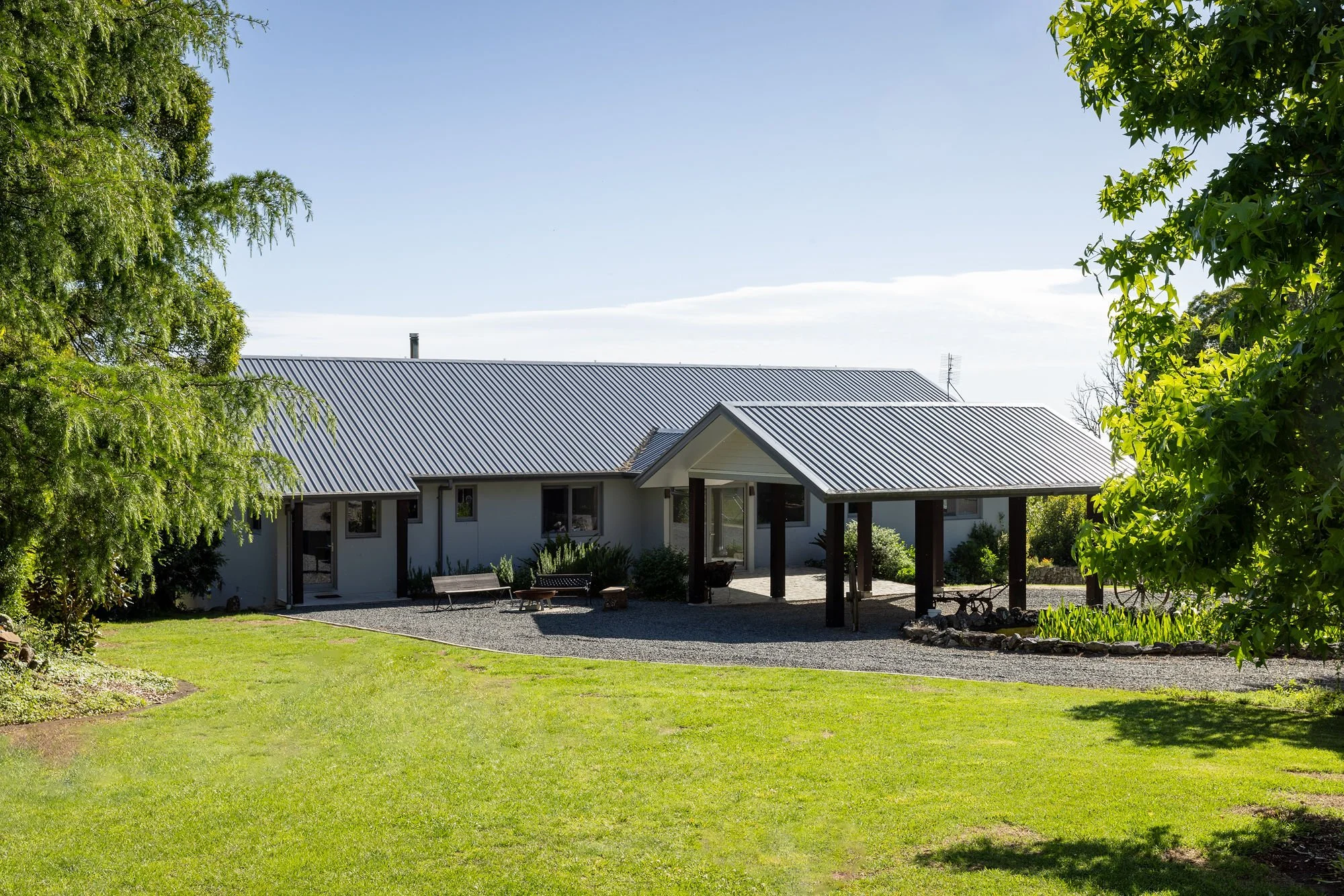 A house with a metal roof seen through trees in a landscaped yard with a green lawn.