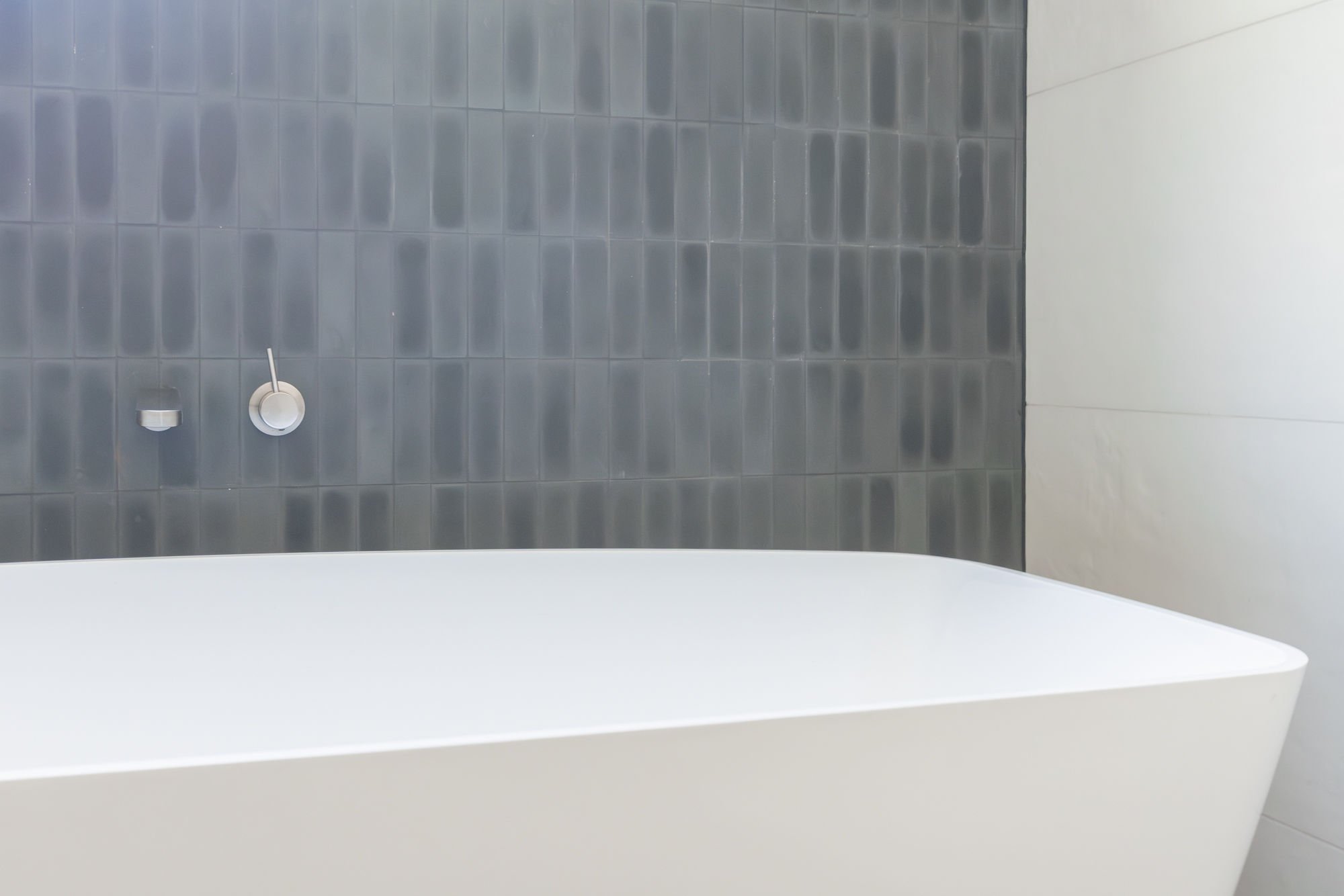 A white bathtub placed against a wall with dark gray tiles, with a silver faucet and a soap dish on the wall.