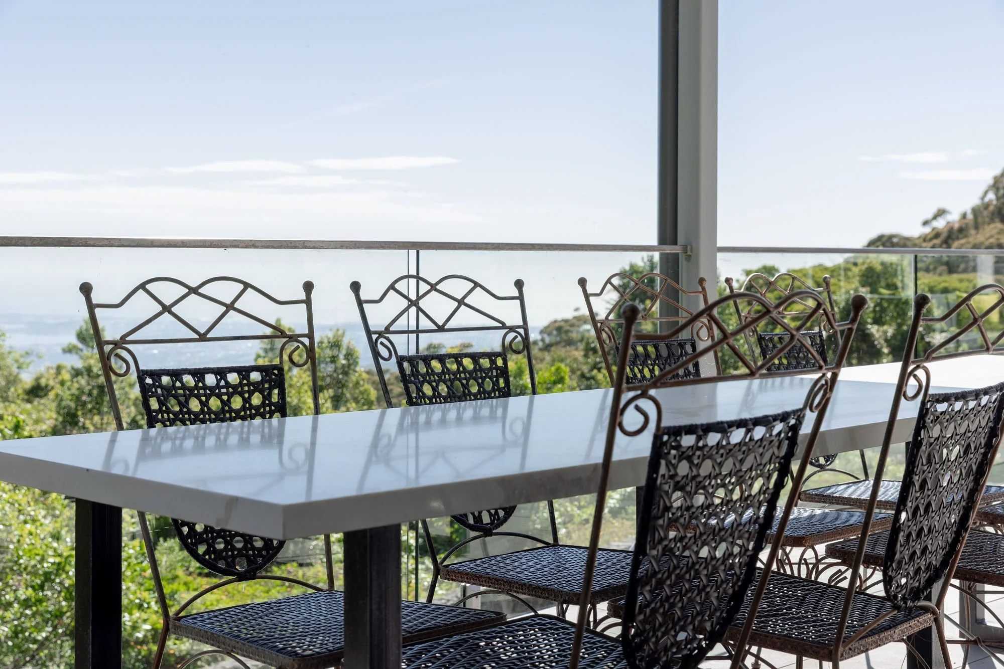 Outdoor dining area with a white table and metal chairs, overlooking a landscape with trees, hills, and a clear sky.
