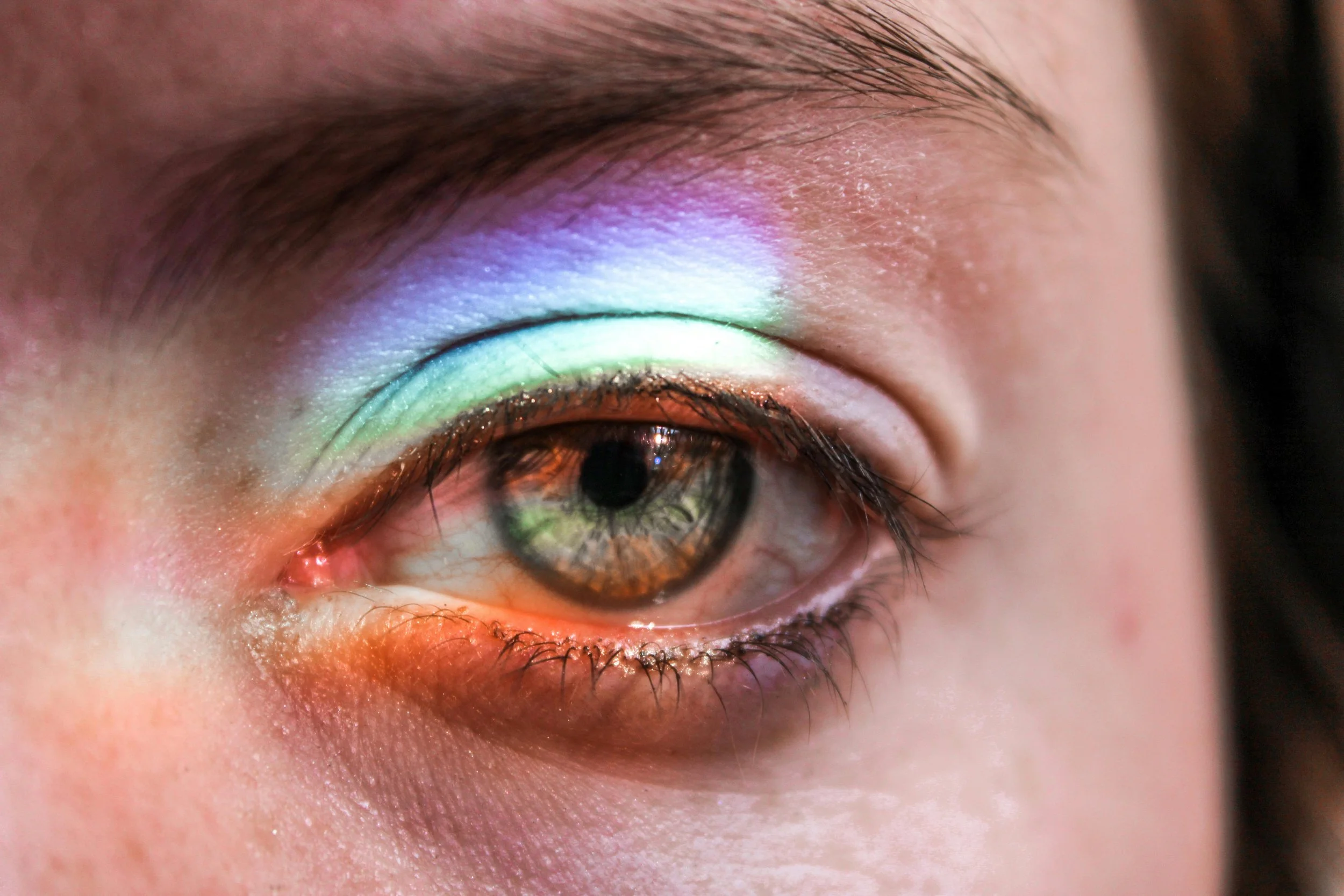 A close-up of a human eye reflecting a rainbow spectrum on the eyelid, showcasing vibrant colors