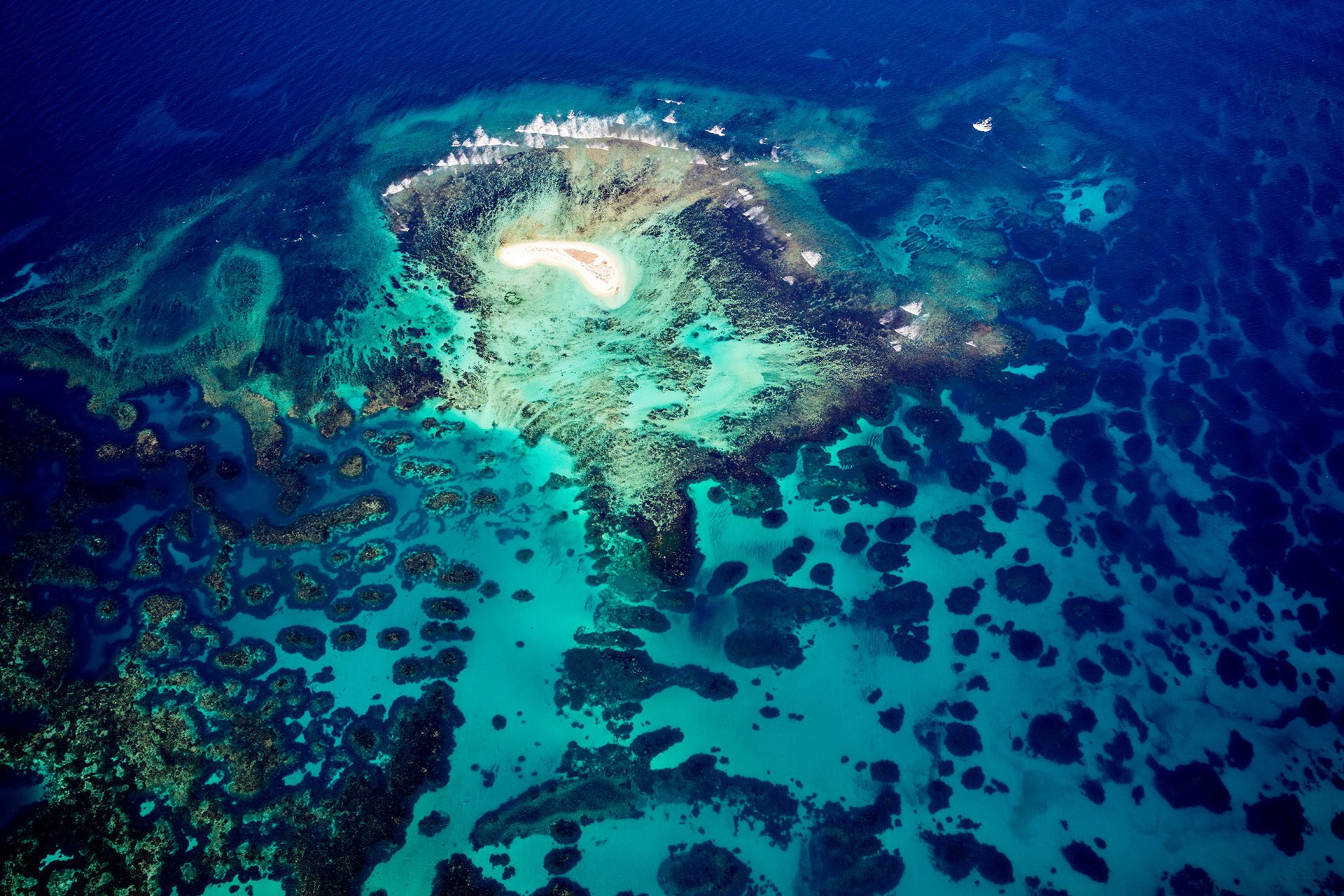 Aerial view of Sandy Island, a small white sand cay surrounded by coral reef and turquoise water in the Houtman Abrolhos Islands, Western Australia.