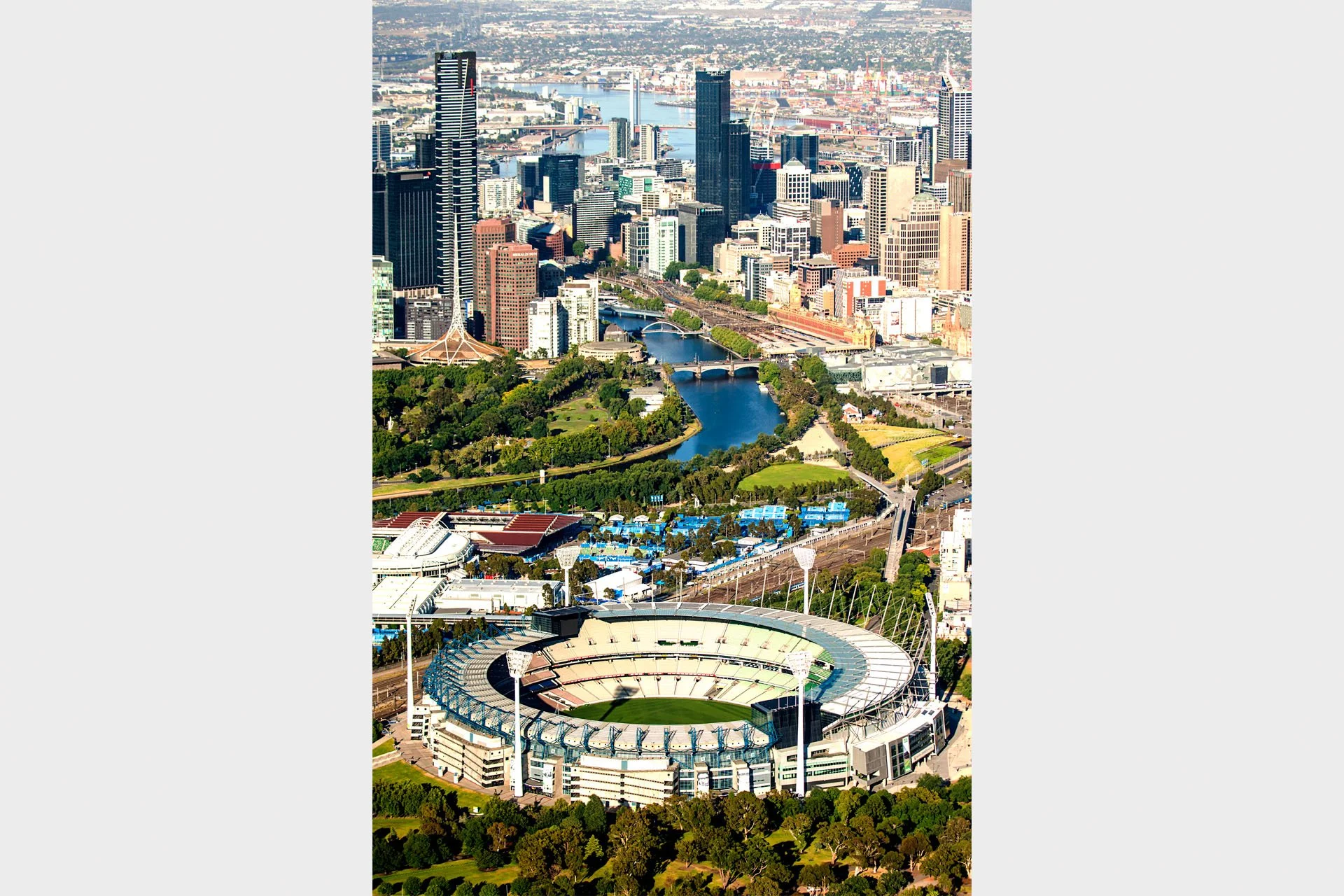 Aerial view over the Melbourne Cricket Ground in Melbourne, Victoria, looking past Melbourne Park and the Yarra River to the city skyline and Port Phillip Bay beyond.